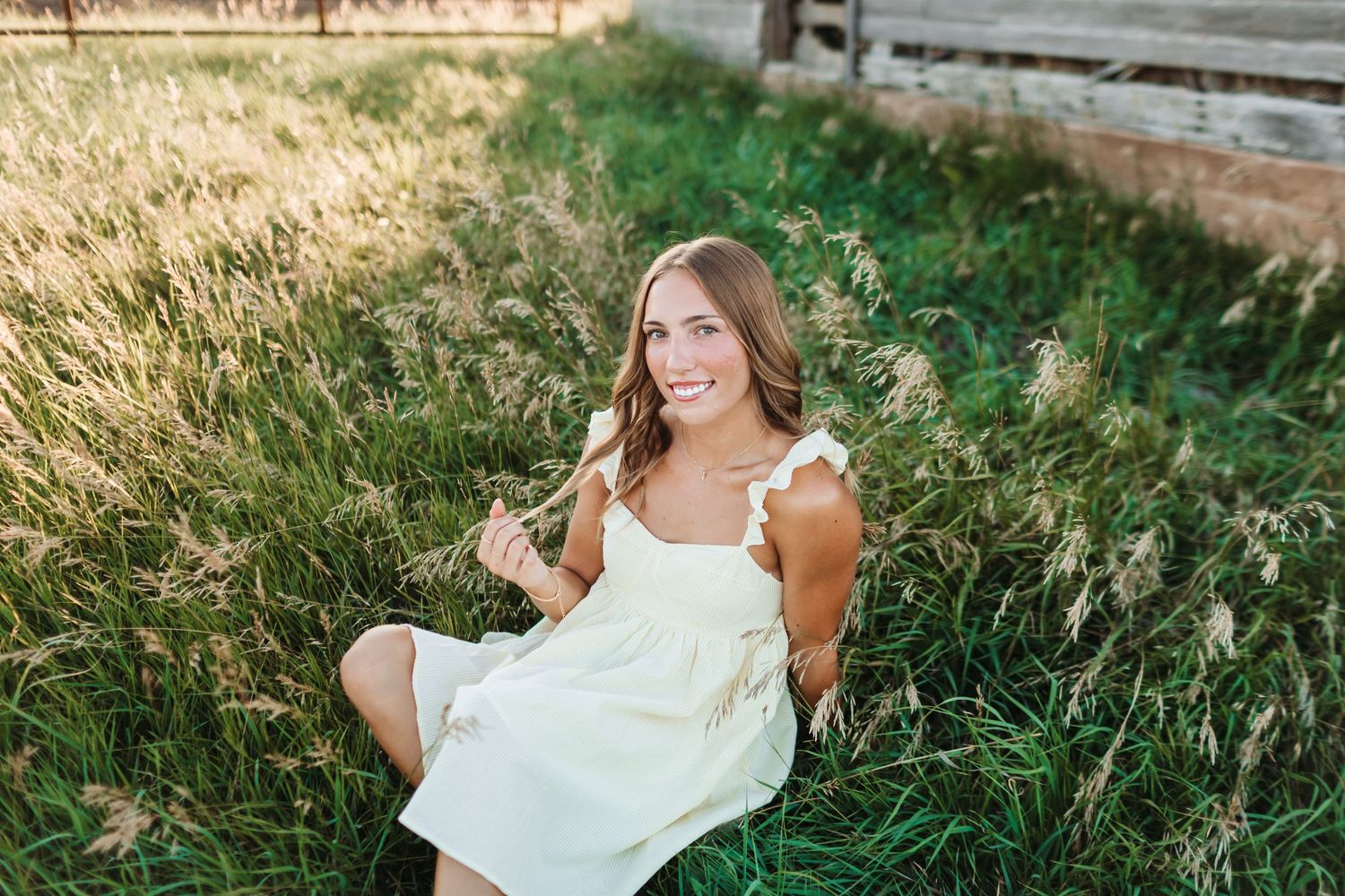 Woman in a yellow dress flowing in summer breeze by old barn.