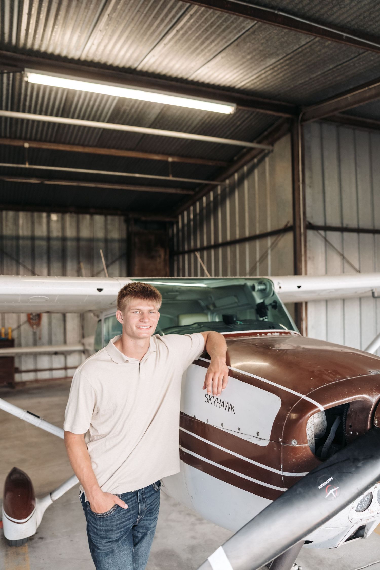Man posed next to a vintage brown and white aircraft displayed in indoor hangar.