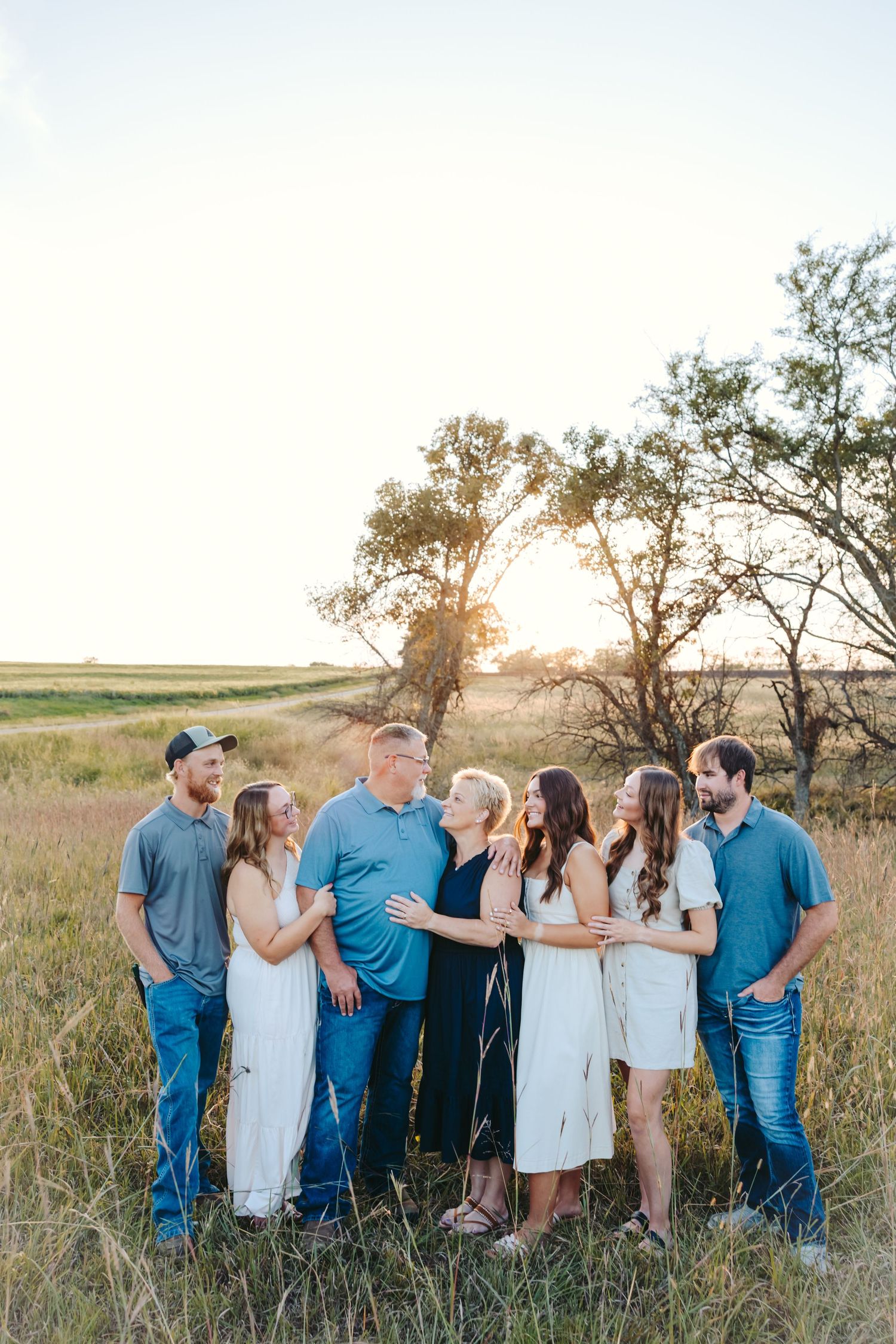 Group photo of family  in coordinating blue and white outfits standing together in a grassy field at sunset.