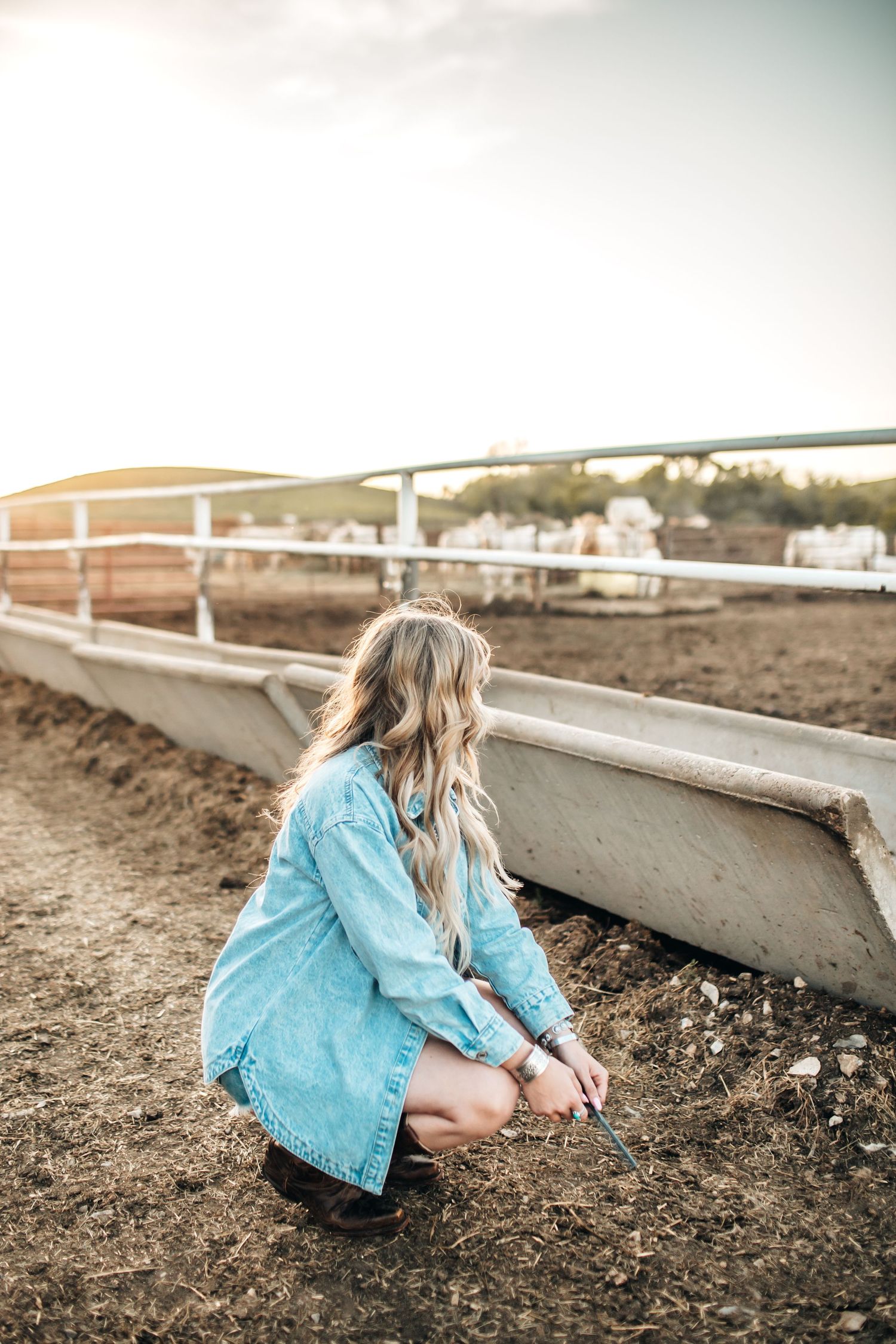 Low angle shot of person in denim examining ground near white fence.