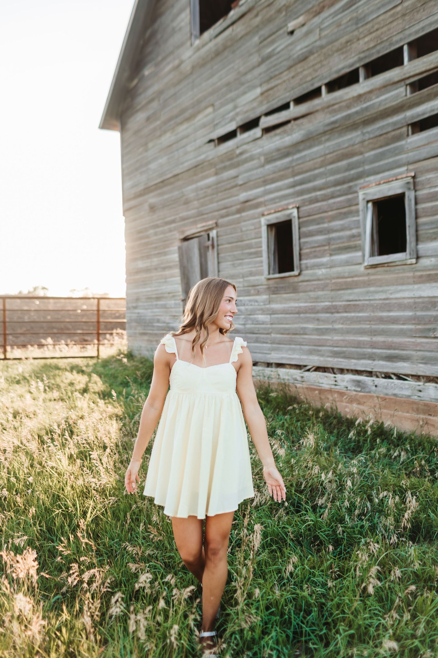 Yellow sundress portrait by weathered wooden barn at golden hour.