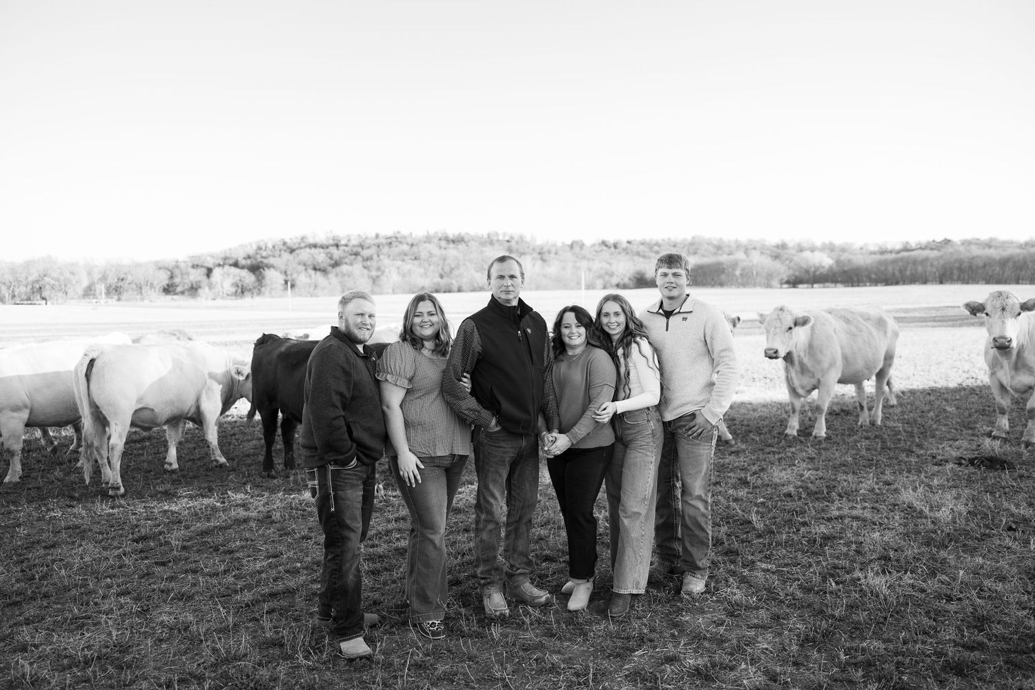Family photo standing in a field with cows visible in the background.