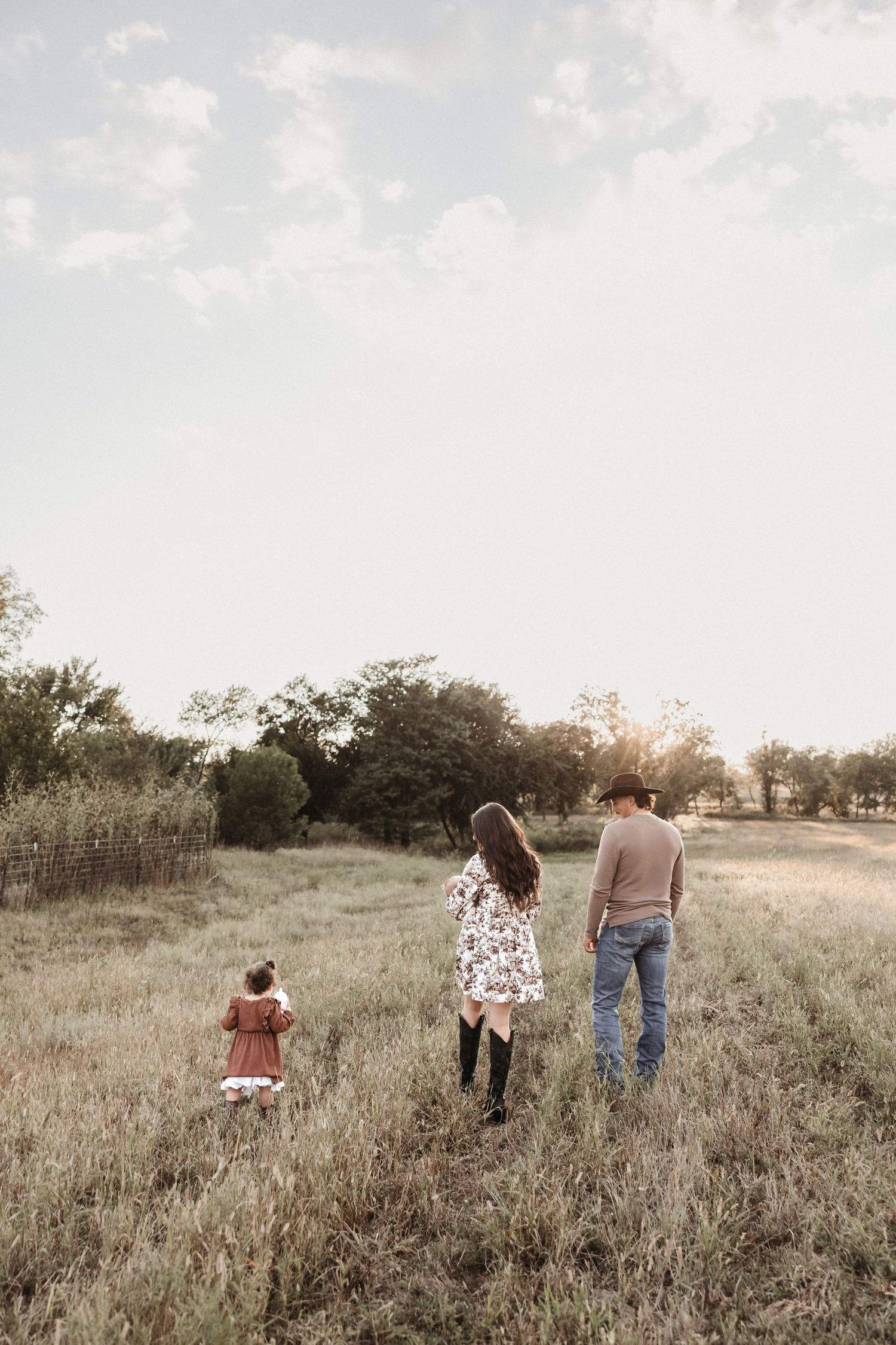 A family walks together through a golden field at sunset, creating a dreamy silhouette against the landscape.