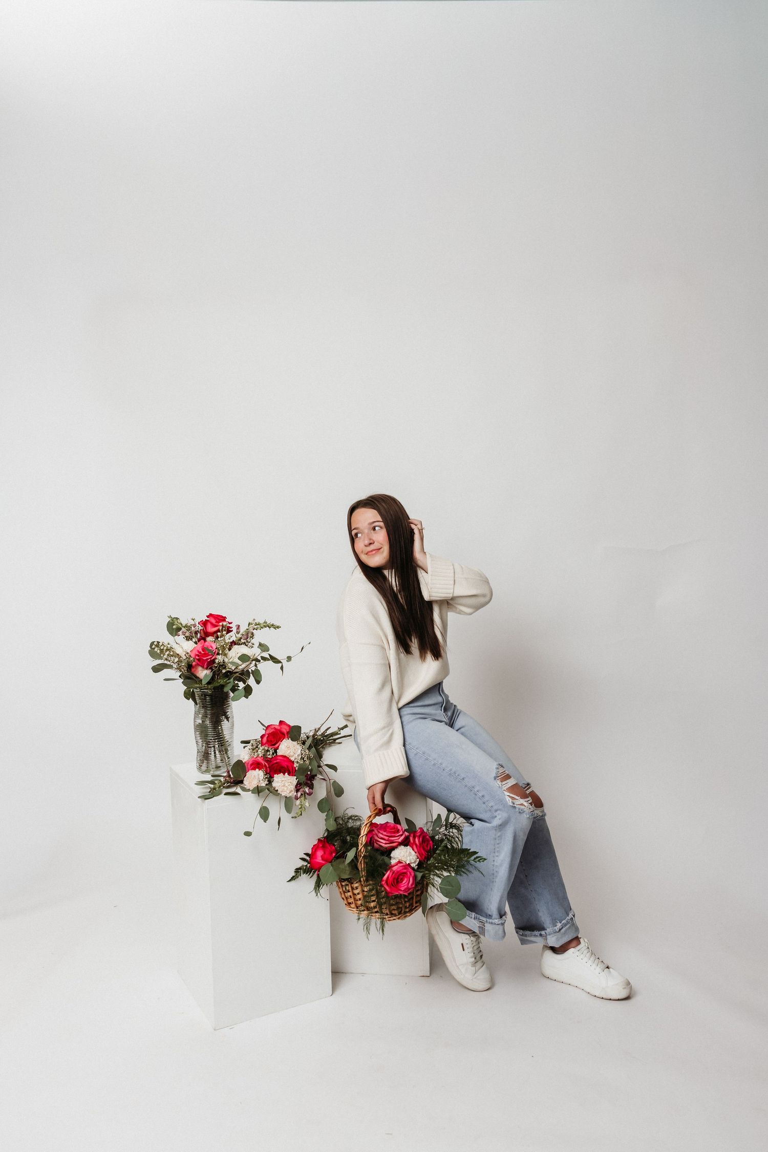 Artistic pose with floral arrangements on white steps against neutral background.