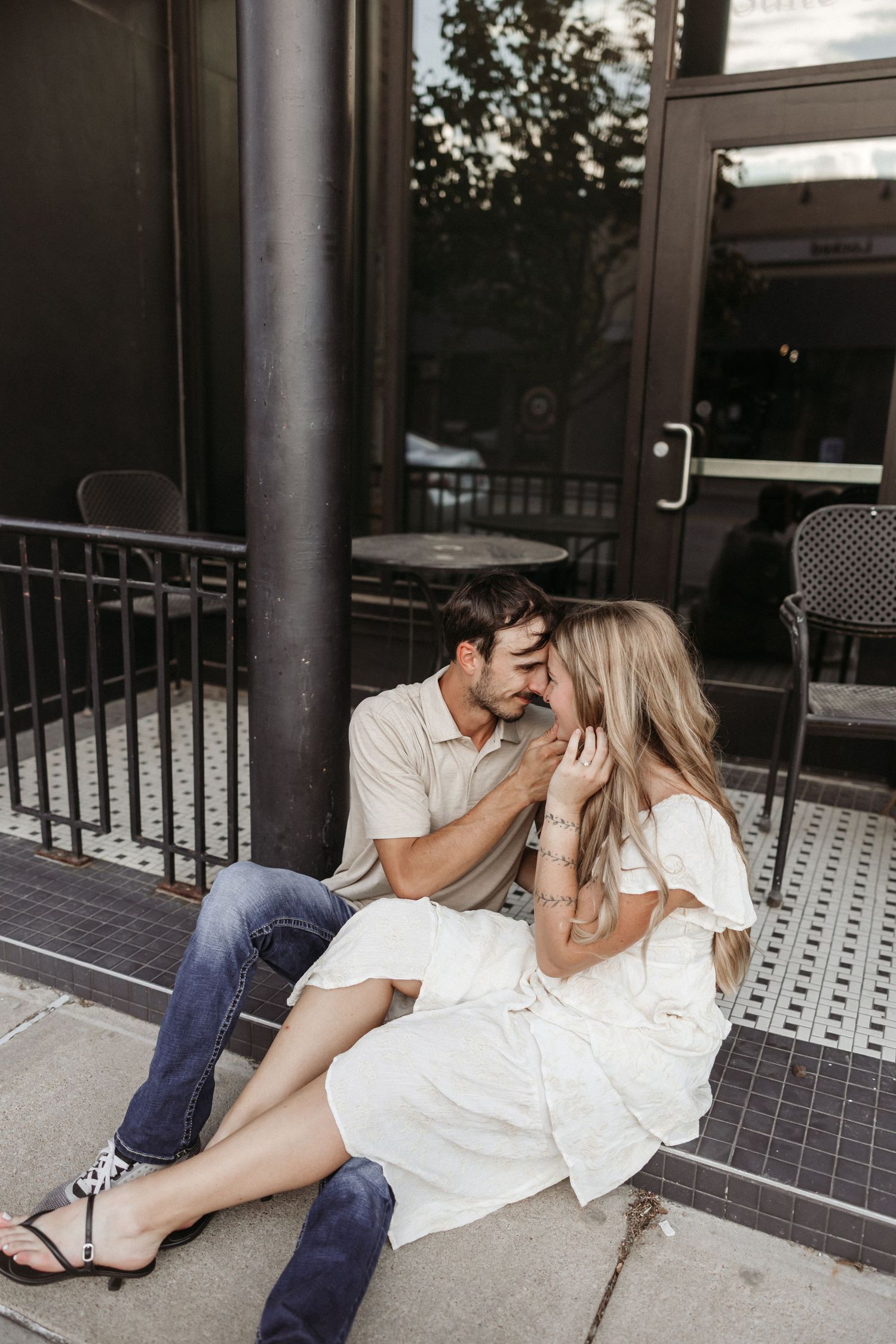 A couple sits intimately together on a tiled porch with black railings.