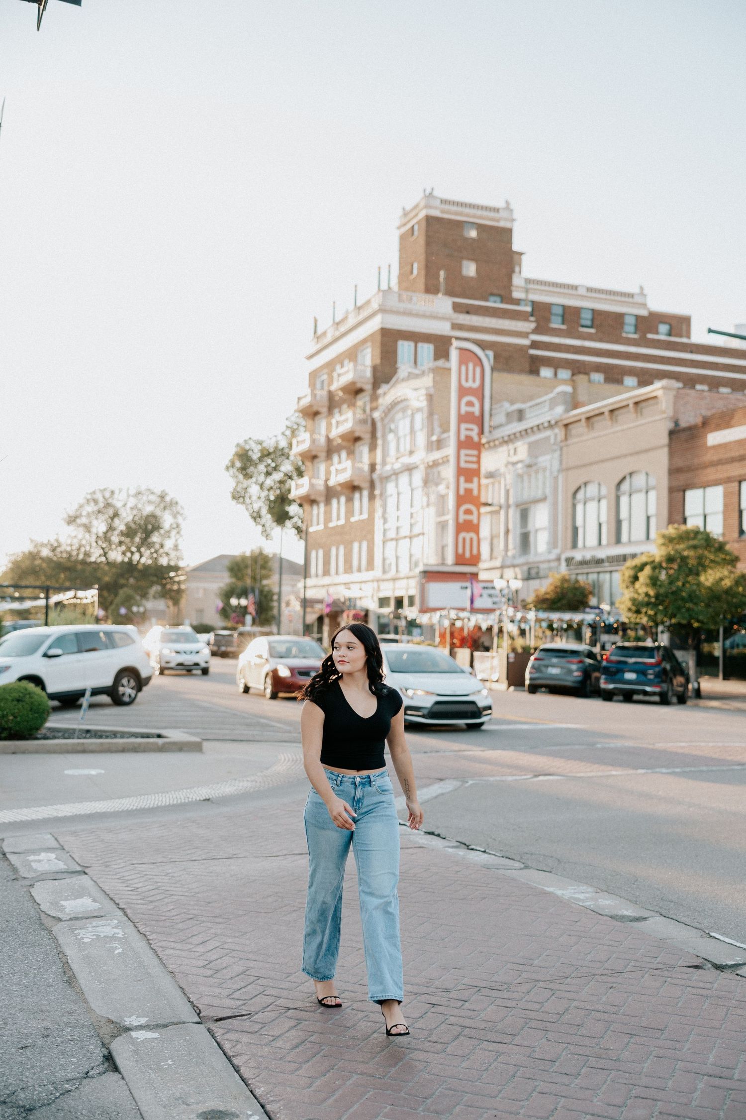 Young woman in black top and jeans walking downtown near the historic Wareham building on a sunny day.