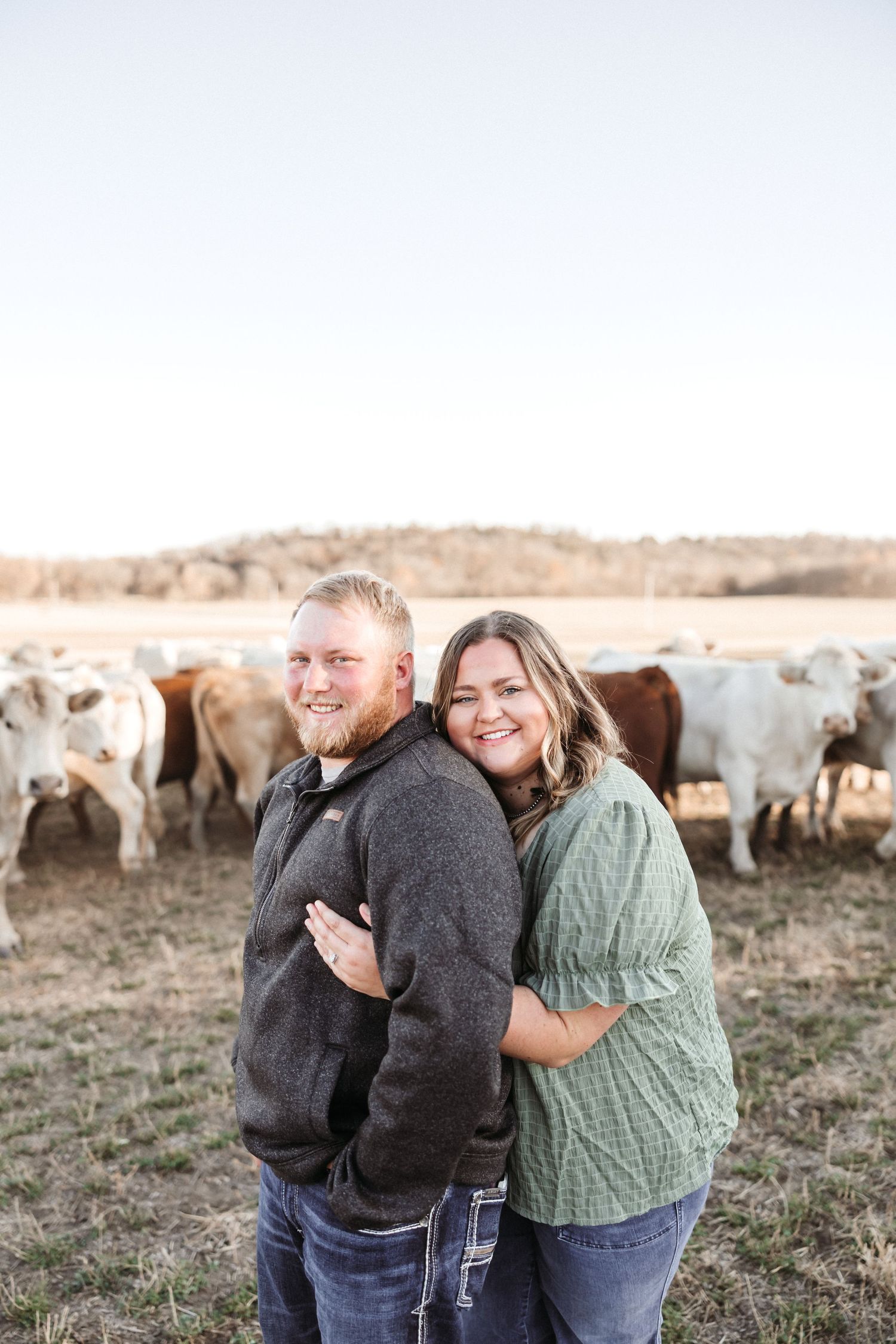 Portrait of couple together in a field with cattle grazing in the background.