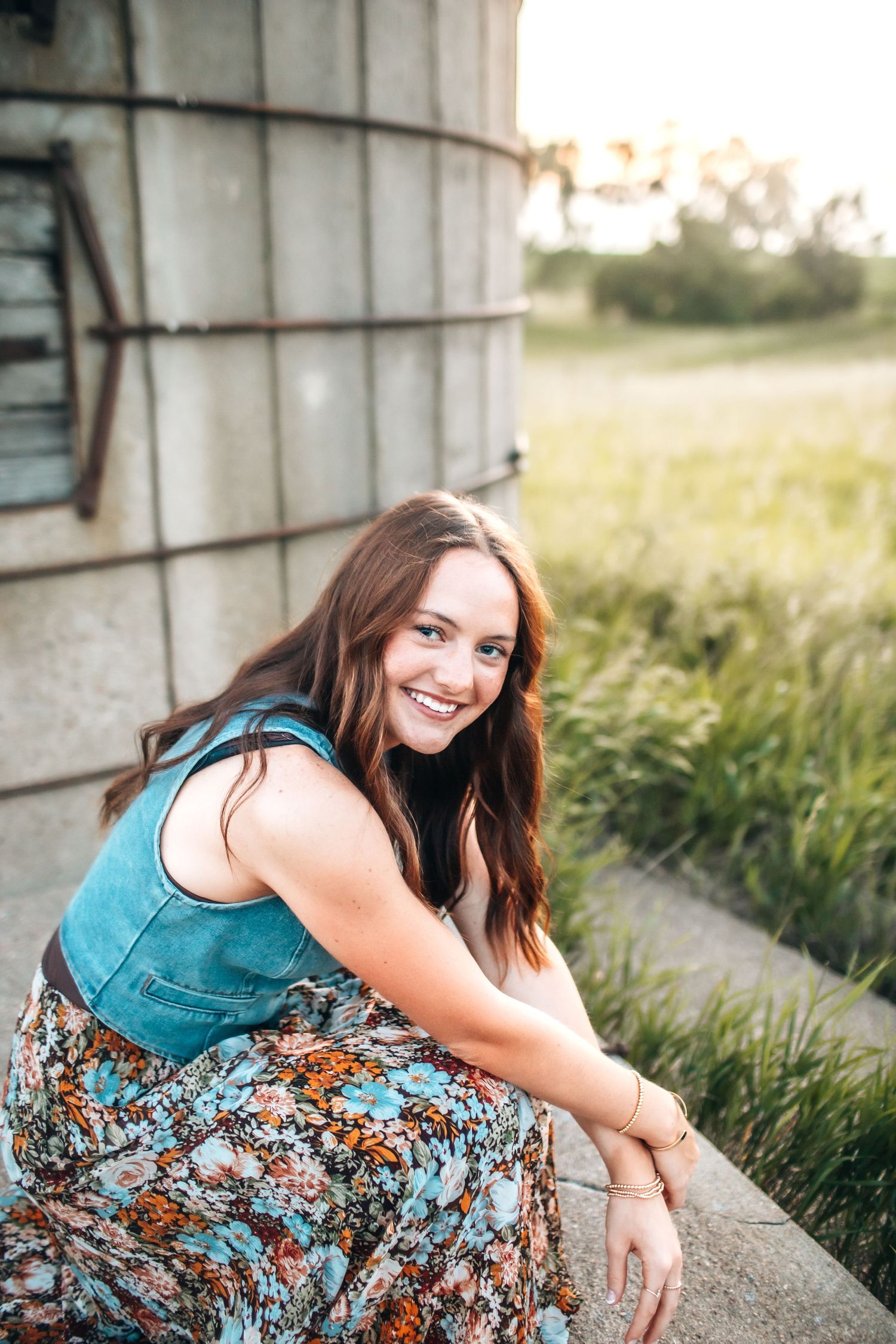 Portrait session near a concrete wall with denim top and floral skirt in natural lighting.