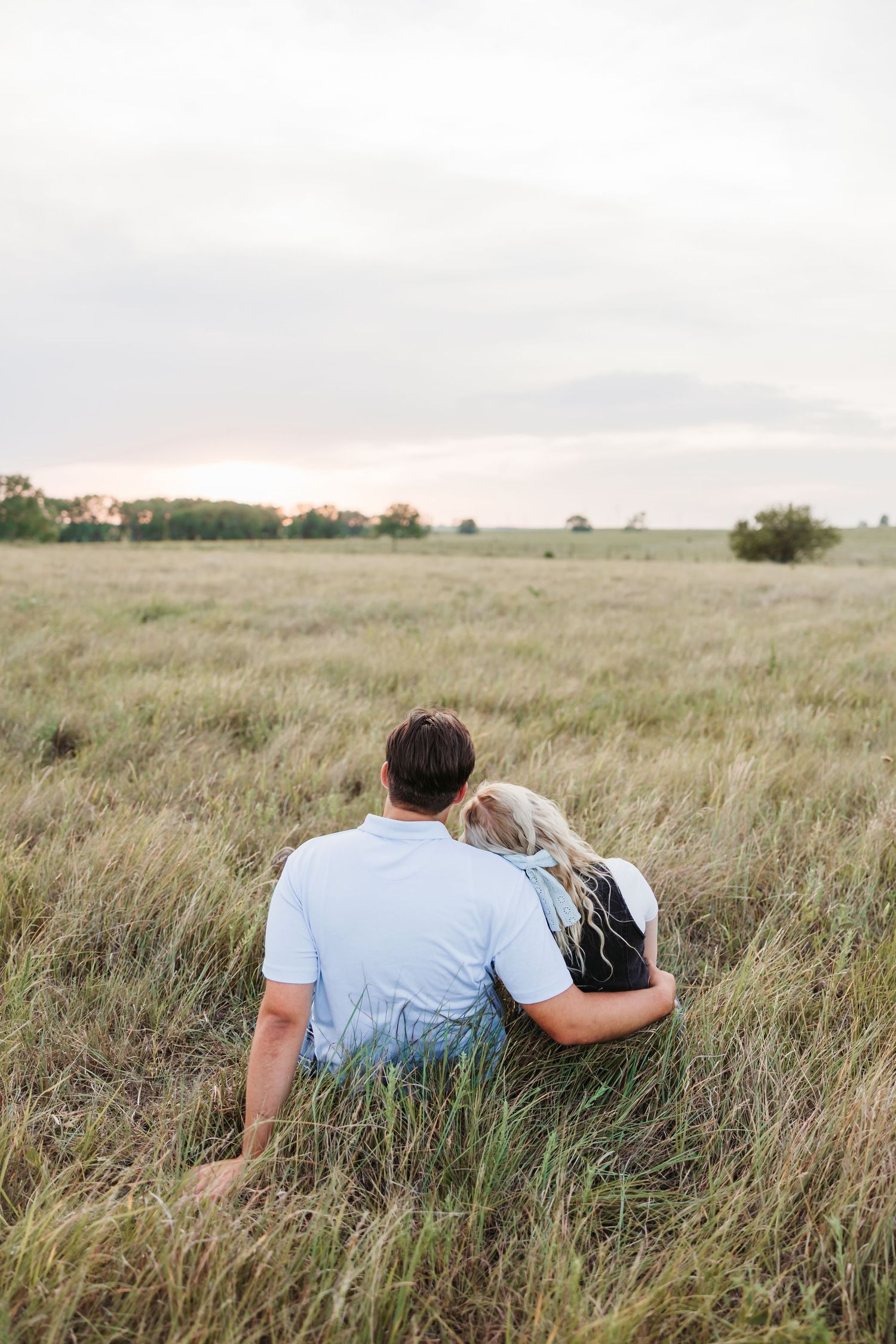 A couple sits together in tall prairie grass during sunset.