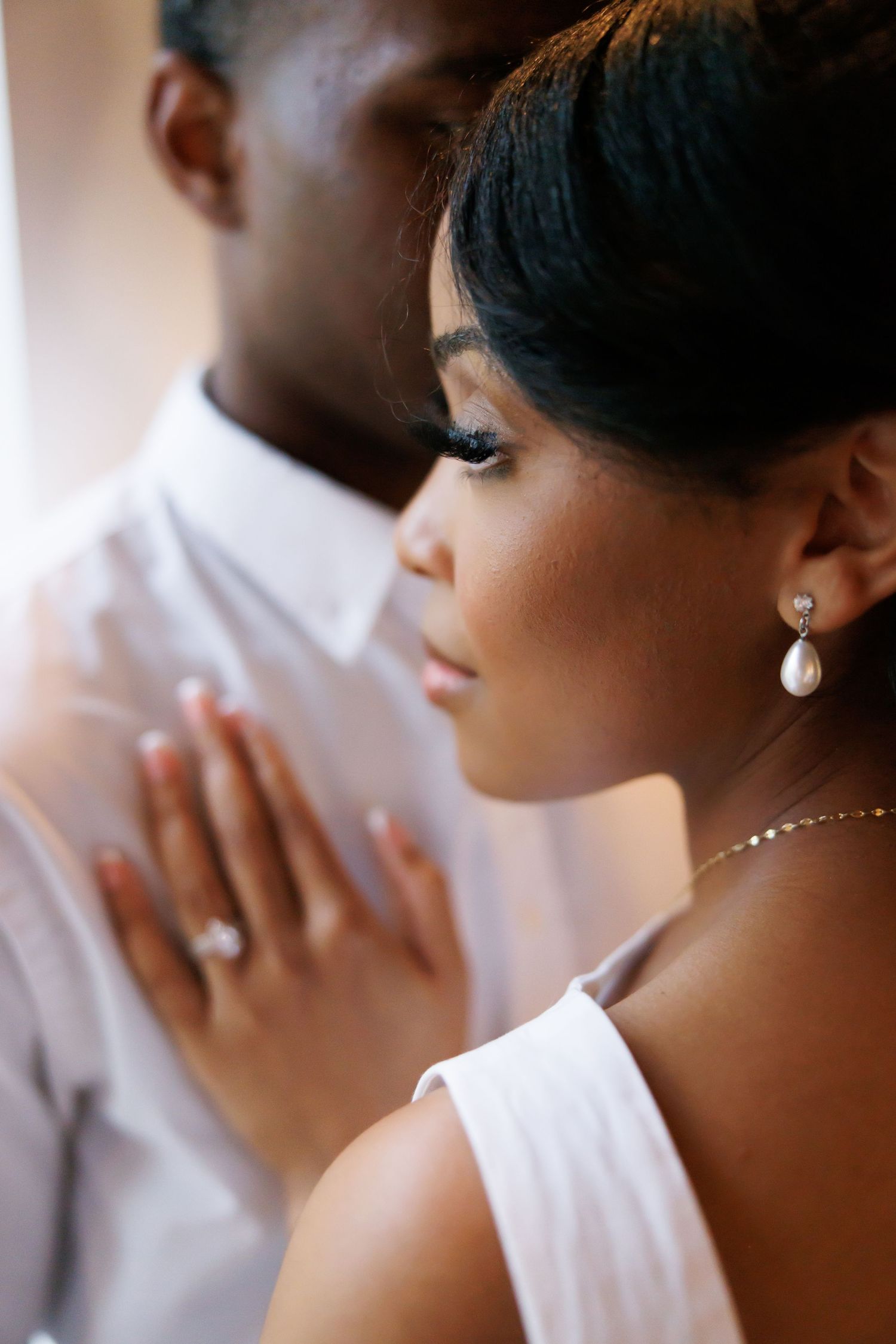 Close-up of an elegant Black couple, bride wearing pearl earrings and diamond ring, gently resting hand on groom's chest.