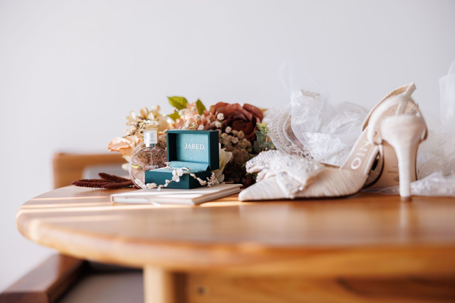 Luxury portrait of Bridal accessories including teal ring box, floral crown, pearl heels, and fan arranged on a wooden table.