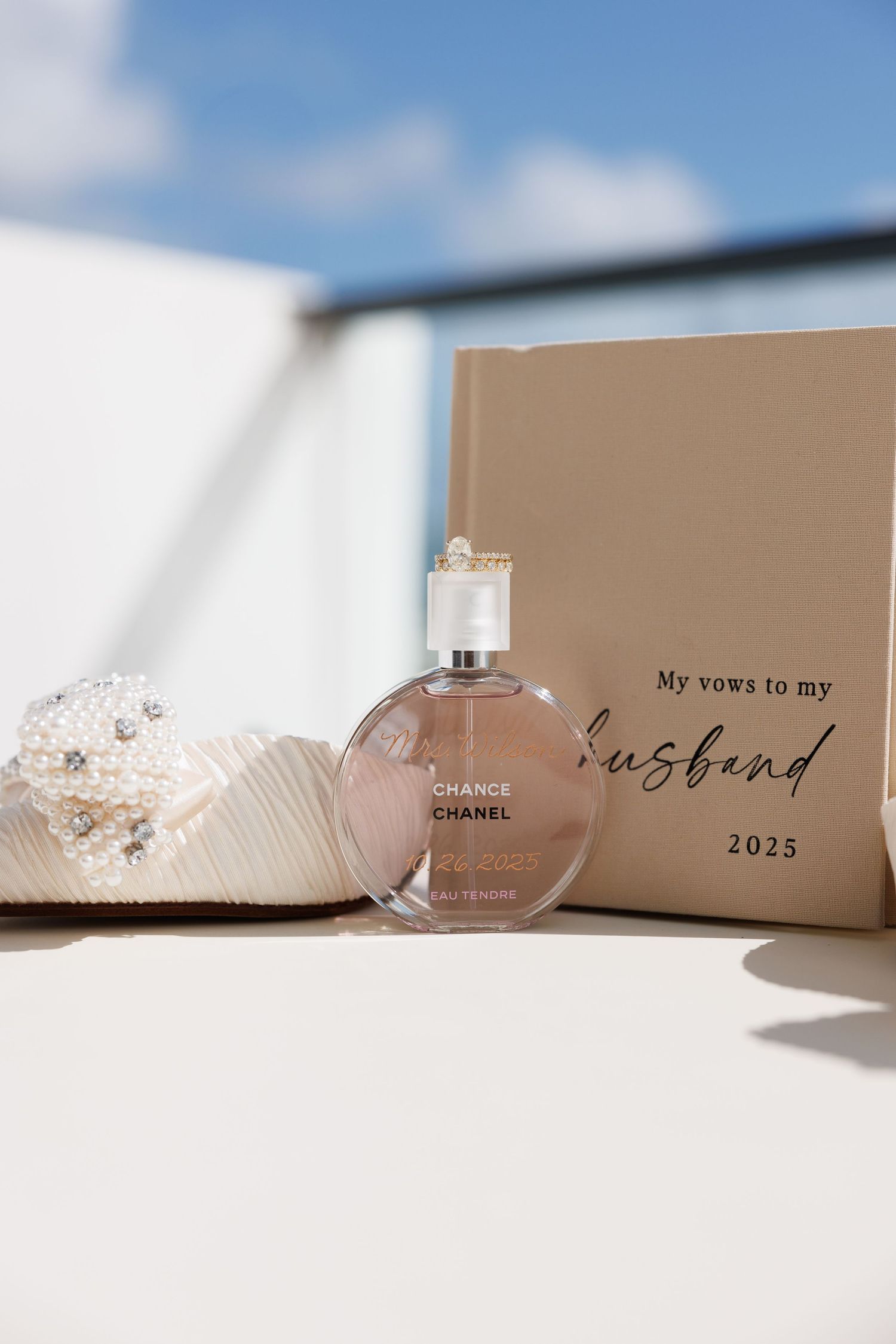 High-end portrait of Chanel Chance perfume bottle beside a wedding vow book and pearl bridal heels outdoors.