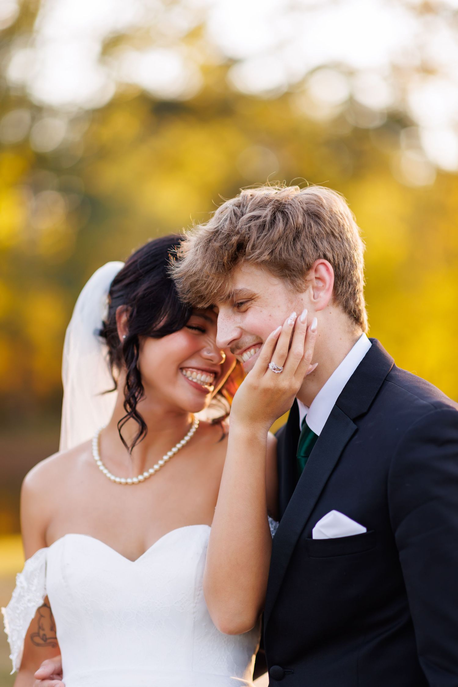 A joyful bride and groom share an intimate moment outdoors, with autumn foliage in the background.