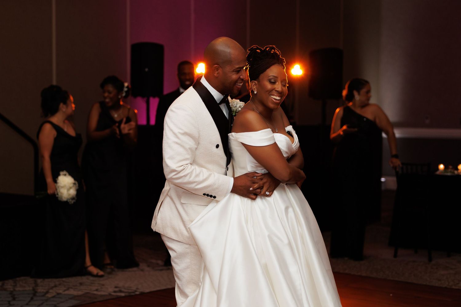 Luxury wedding picture of Bride and groom share their first dance in a ballroom with purple ambient lighting.