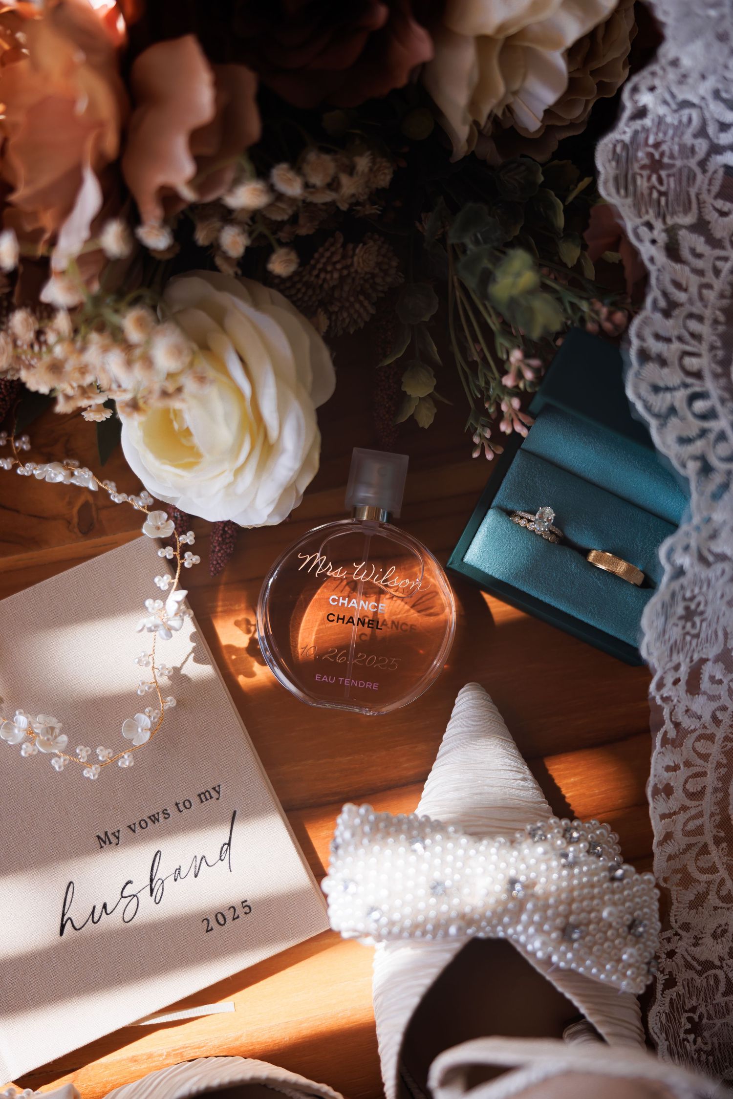 Bridal picture of flat lay with vows book, Chanel perfume, rings, bouquet, and pearl accessories.