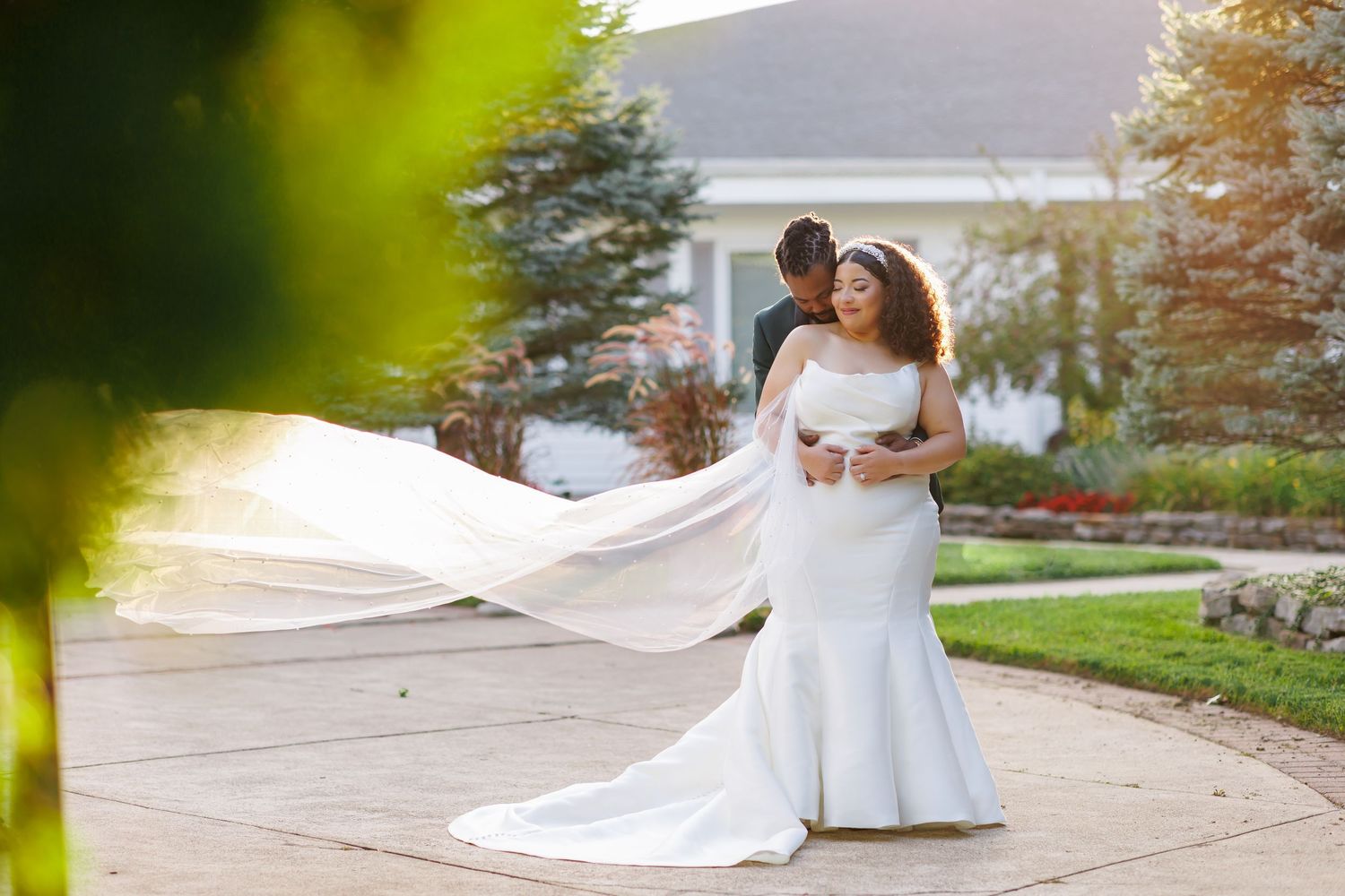 Luxury wedding picture of Bride and groom embrace on garden path as her cathedral veil flows dramatically in the breeze.