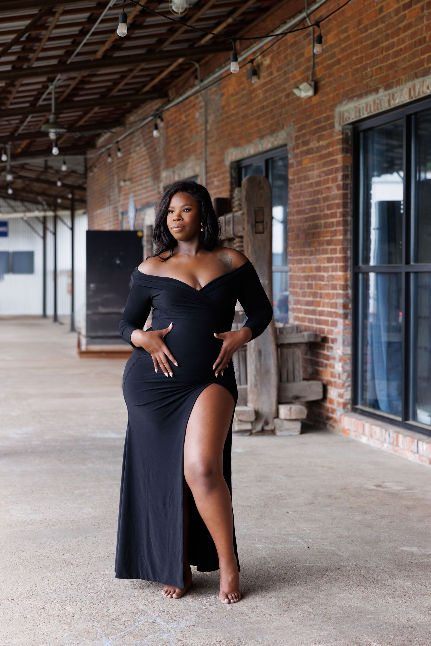Luxury wedding picture of A pregnant Black woman poses gracefully in a black off-shoulder gown inside a rustic brick warehouse venue.
