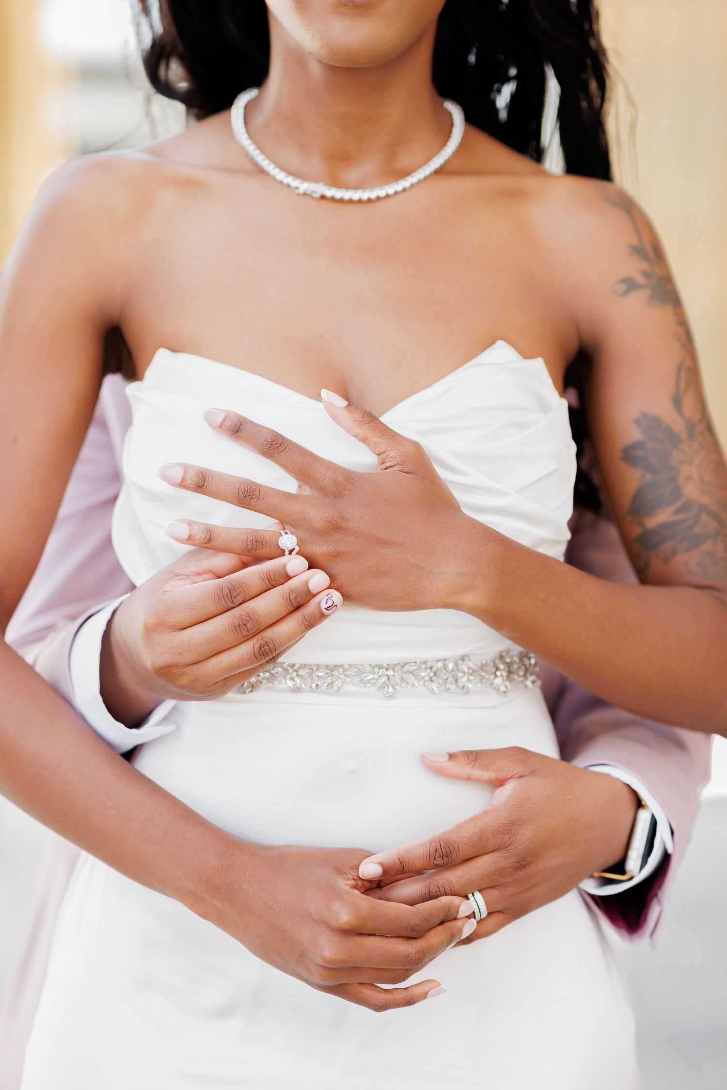 Luxury wedding picture of A bride in a white strapless gown with a crystal belt holds hands with her groom showing wedding rings.