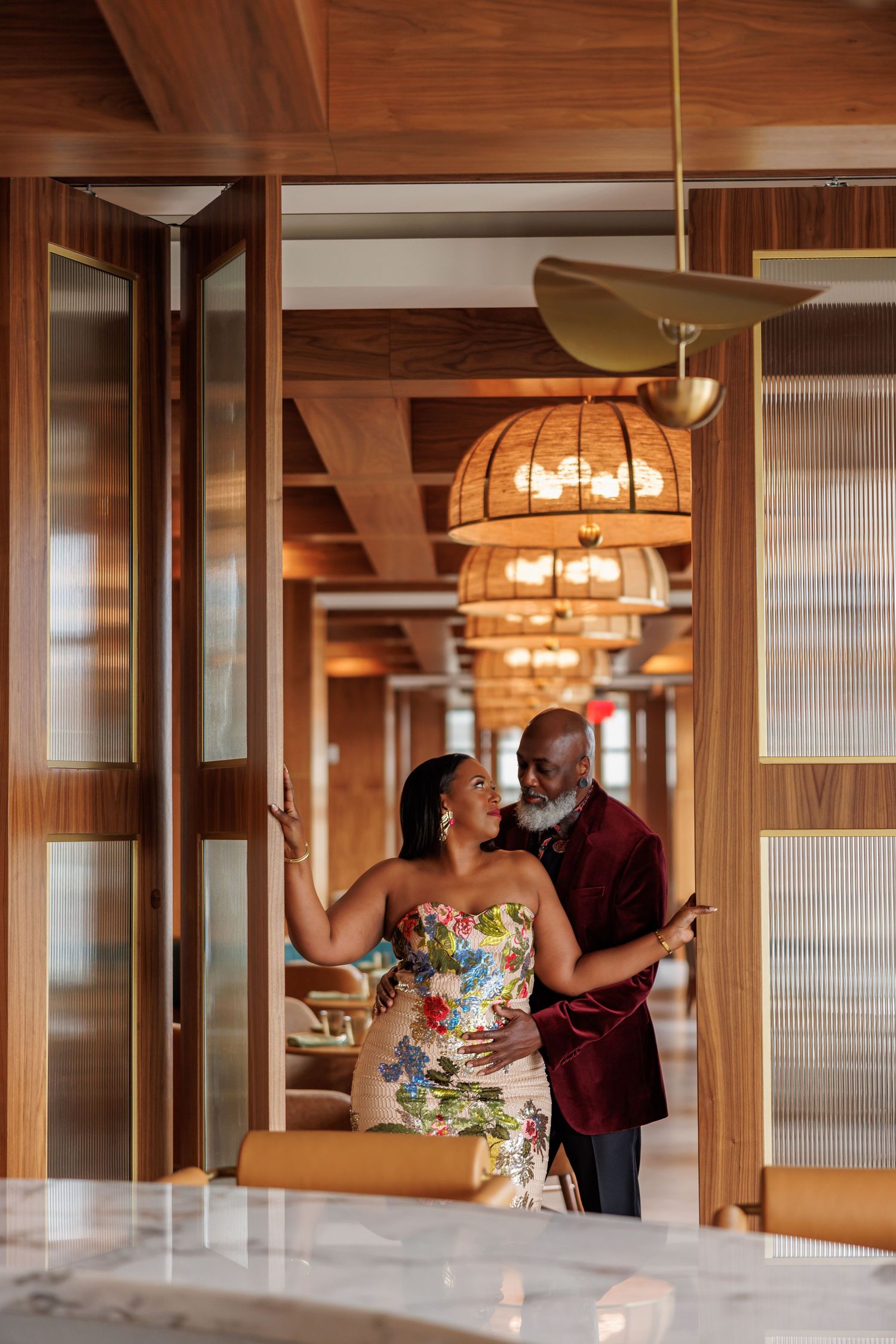 Elegant picture of couple admiring a luxurious restaurant interior with warm wooden decor and chandeliers.