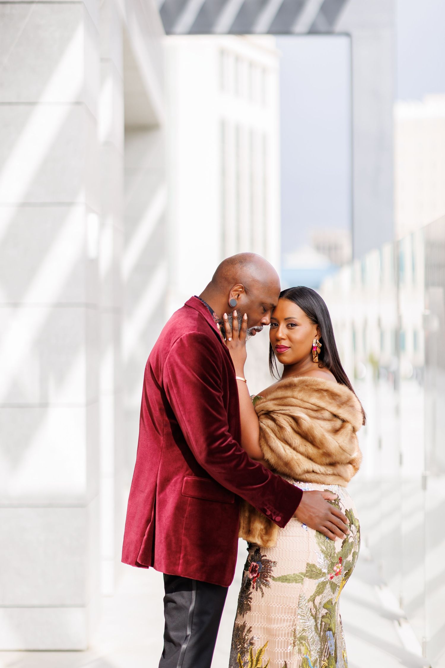 Elegant picture of Black couple in luxury attire sharing romantic moment outdoors, man in burgundy velvet blazer.
