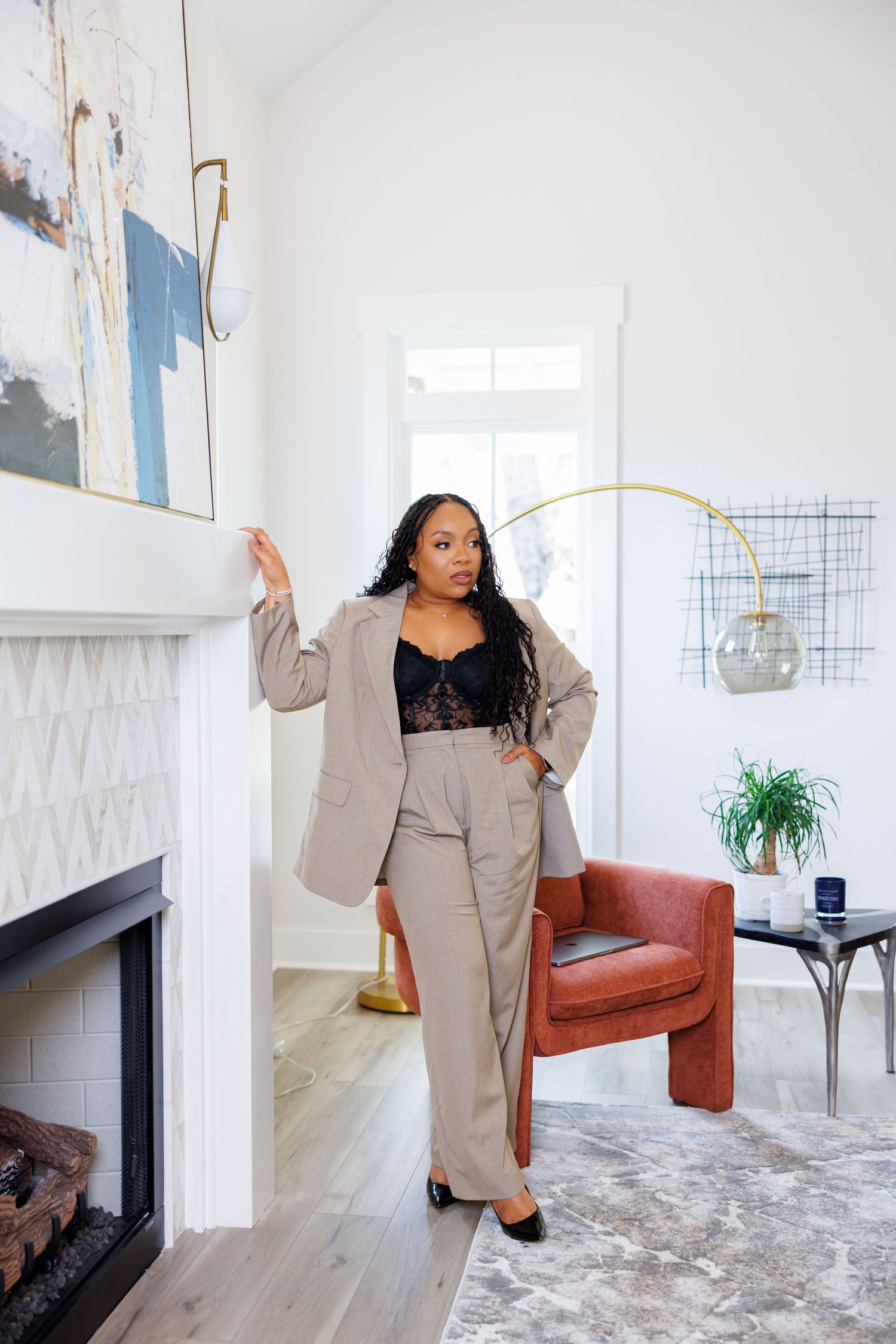 Picture of woman in beige blazer suit posing by fireplace in modern white living room.