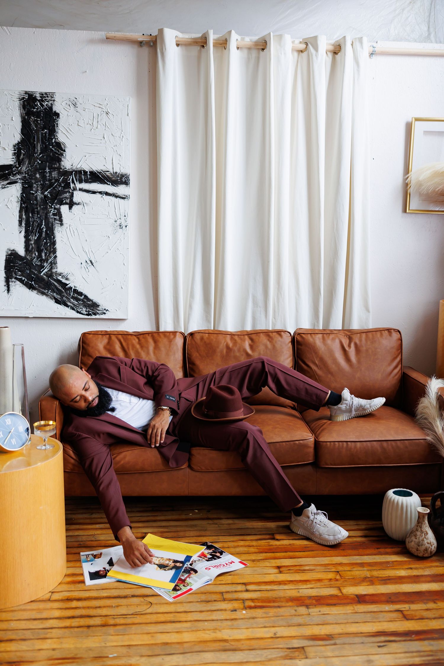 Black man in burgundy suit relaxes on leather sofa browsing magazines on hardwood floor picture
