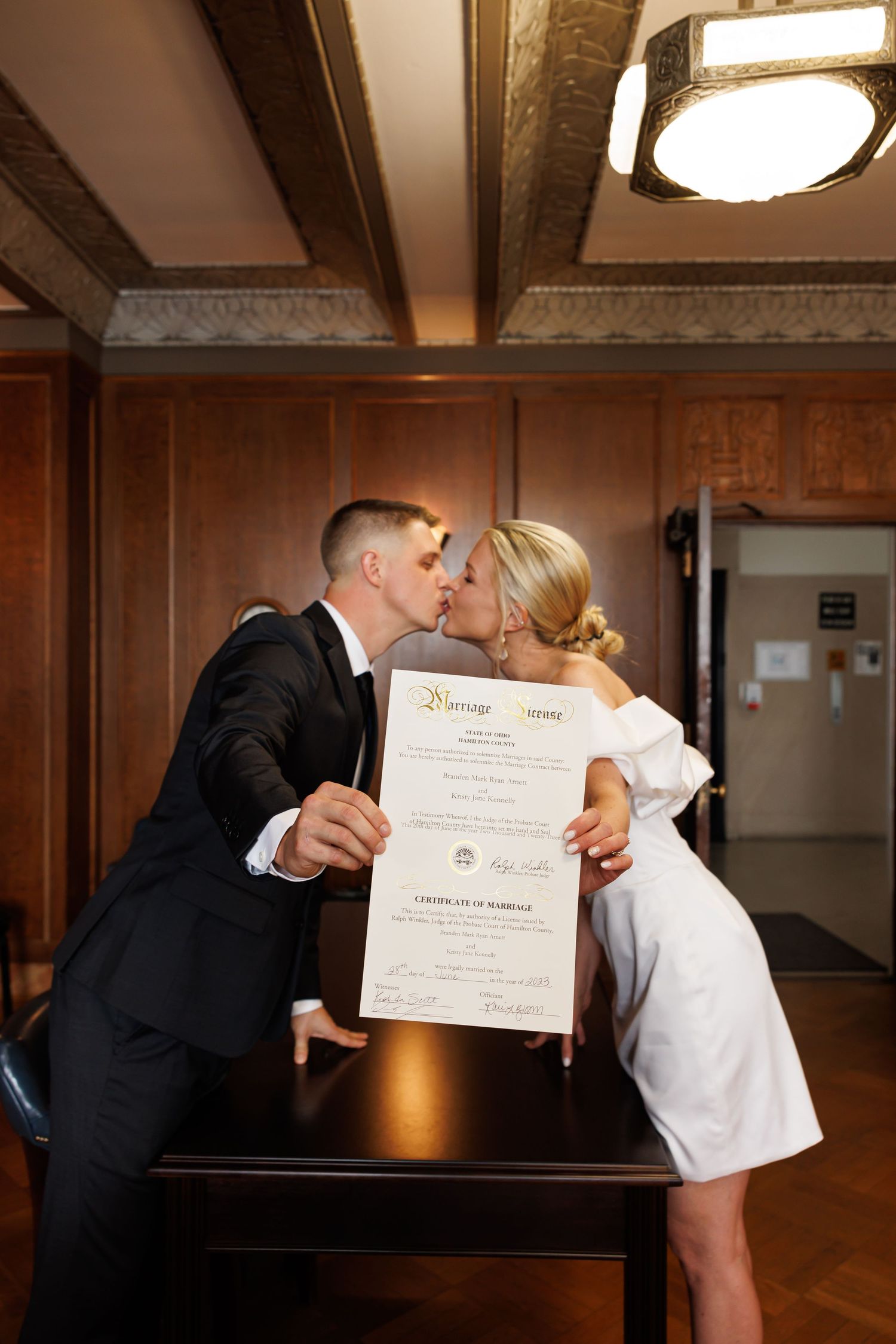 Timeless portrait of Newlyweds kiss while holding their marriage certificate at a courthouse wedding ceremony.