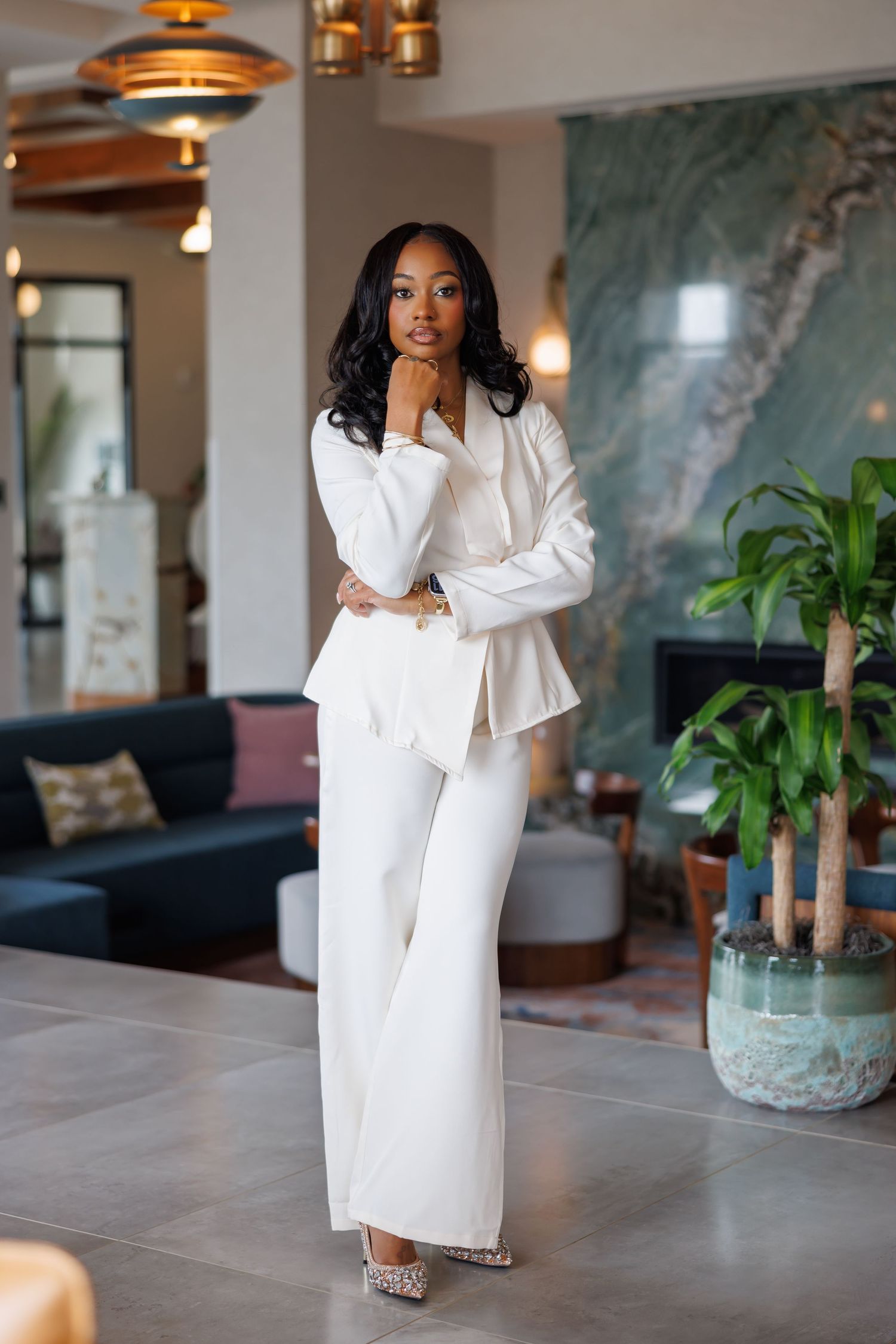Elegant picture of Confident Black woman poses in white blazer and wide-leg pants suit in modern upscale interior.