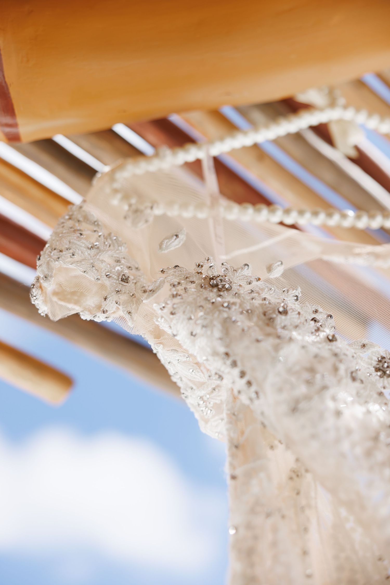 Luxury wedding picture of Close-up of beaded bridal gown bodice hanging on a wooden hanger against a blue sky.