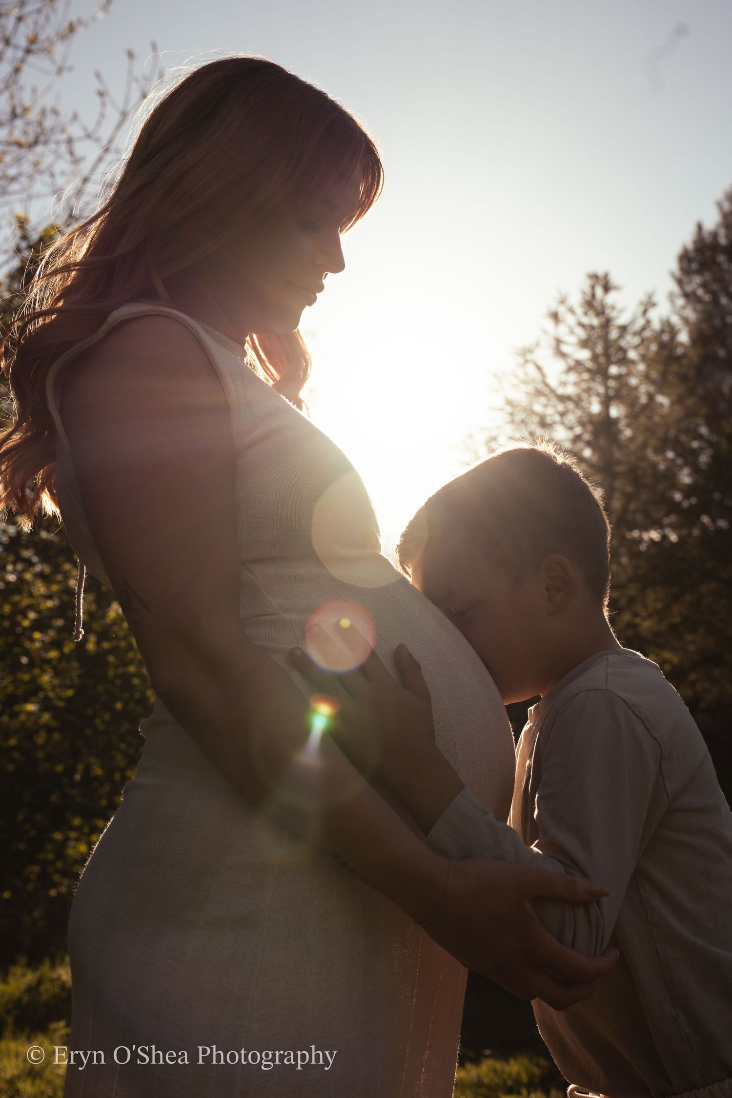 Child kissing pregnant mother’s belly during maternity photo session