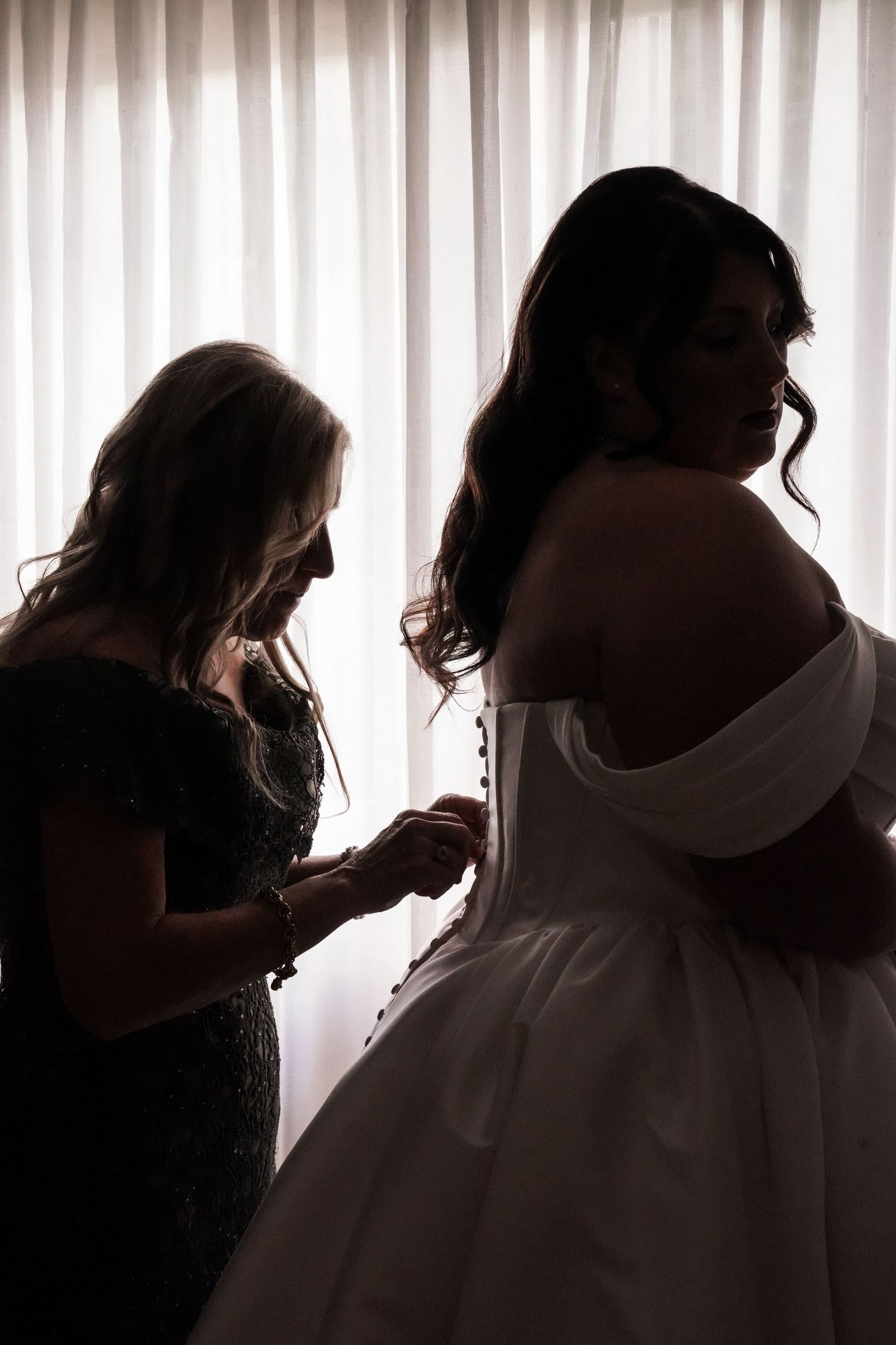 mom helping daughter do up wedding dress