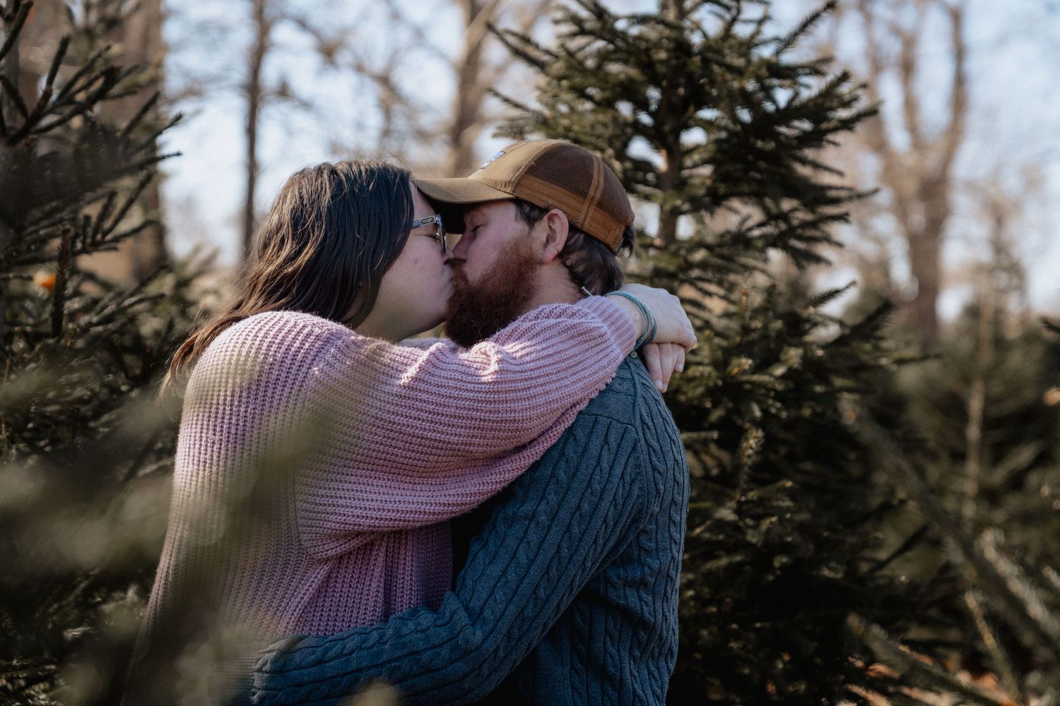 Romantic moment of couple kissing among evergreen trees at tree farm