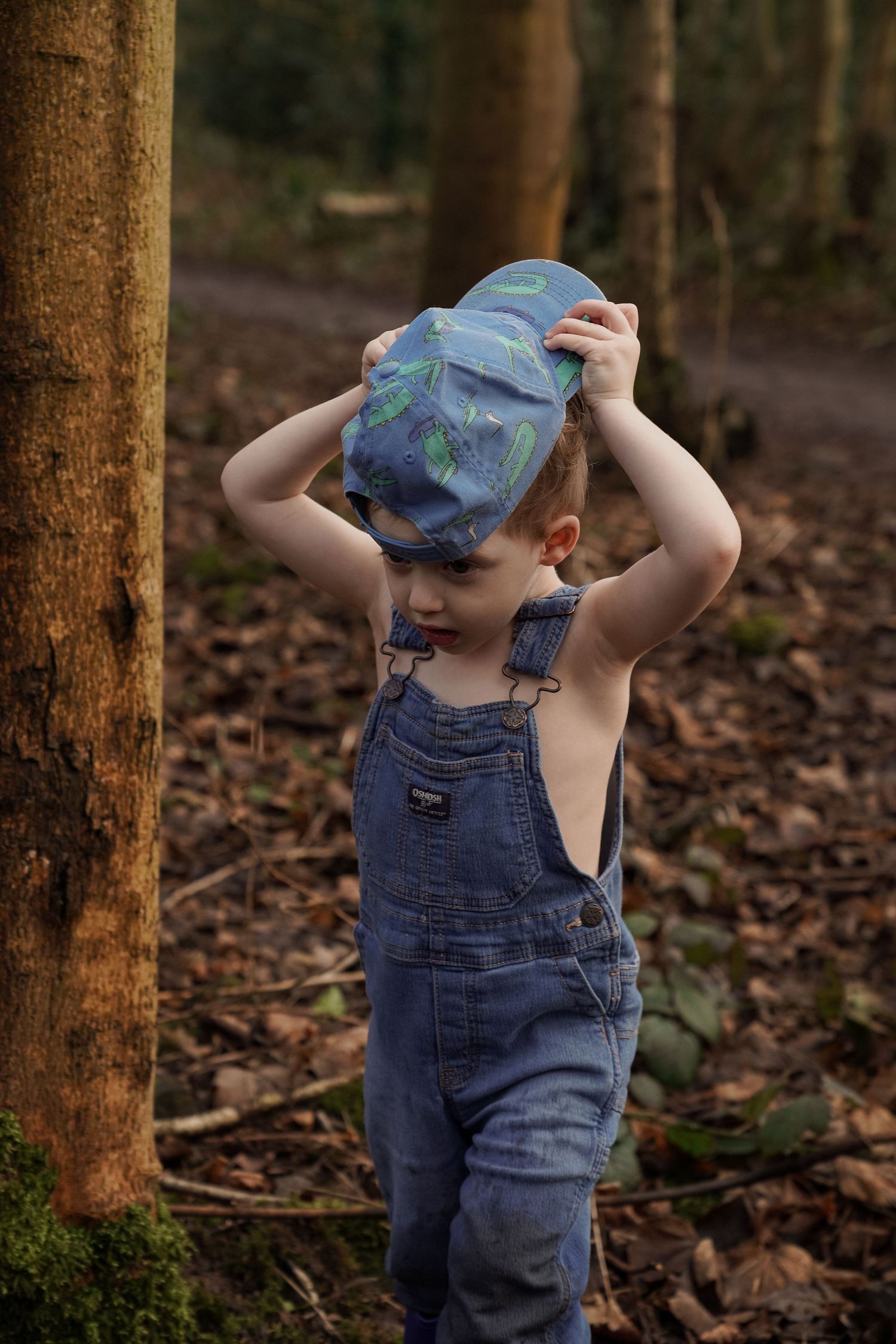 Child putting on a hat while wearing overalls during muddy spring photo session