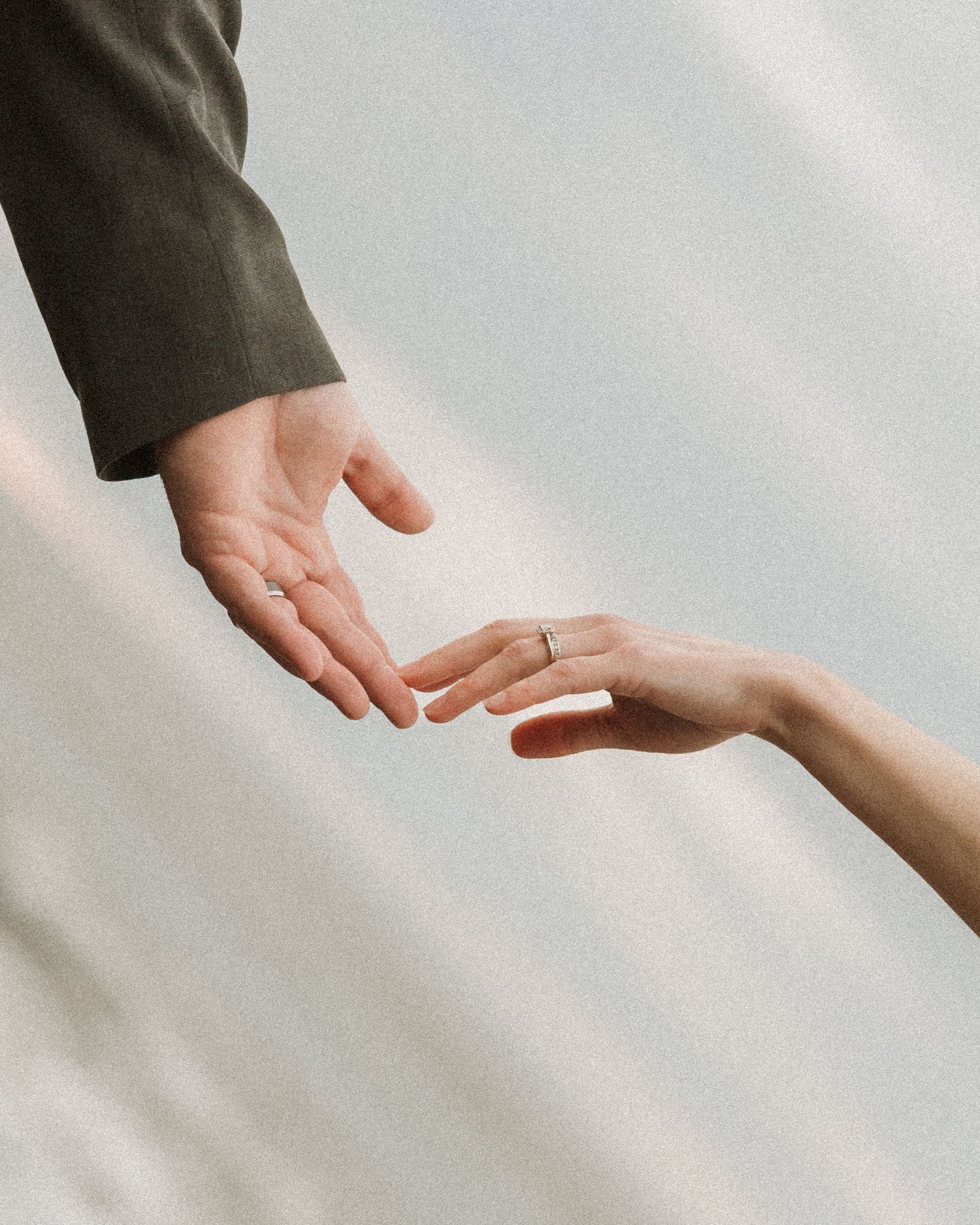 Close-up of bride and groom gently reaching for each other's hands, bride wearing a wedding ring.