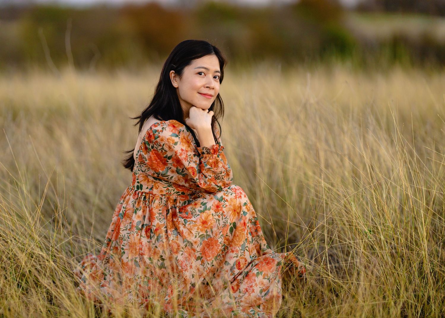 A flowing floral dress stands out against a golden field of tall grass at sunset.