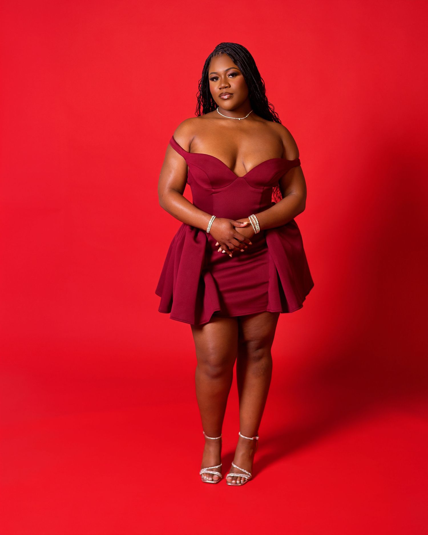 A woman in a burgundy dress poses confidently against a vibrant red backdrop in a fashion photoshoot series.