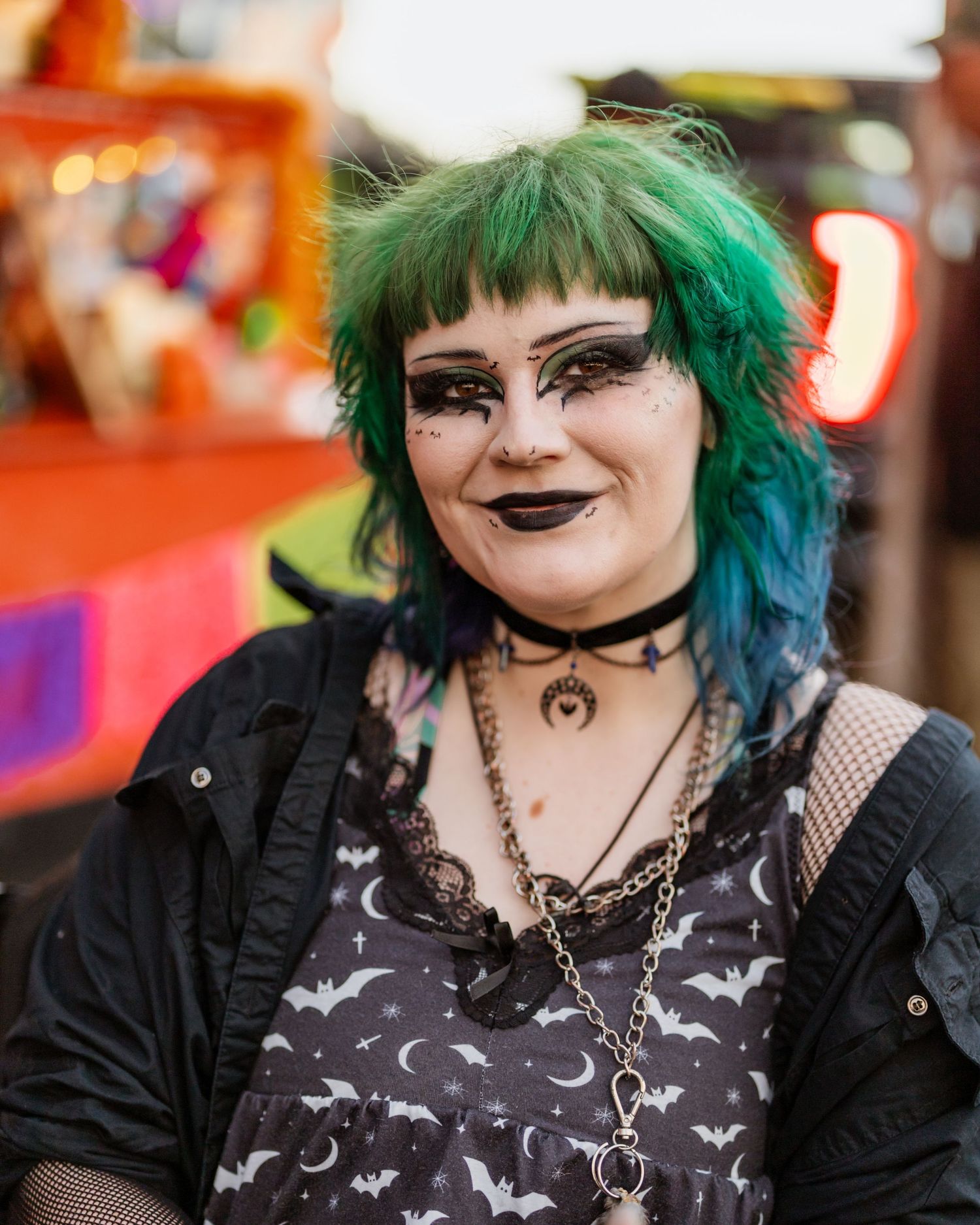 Person with vibrant green and blue hair wearing gothic style clothing with moon pattern against orange background.