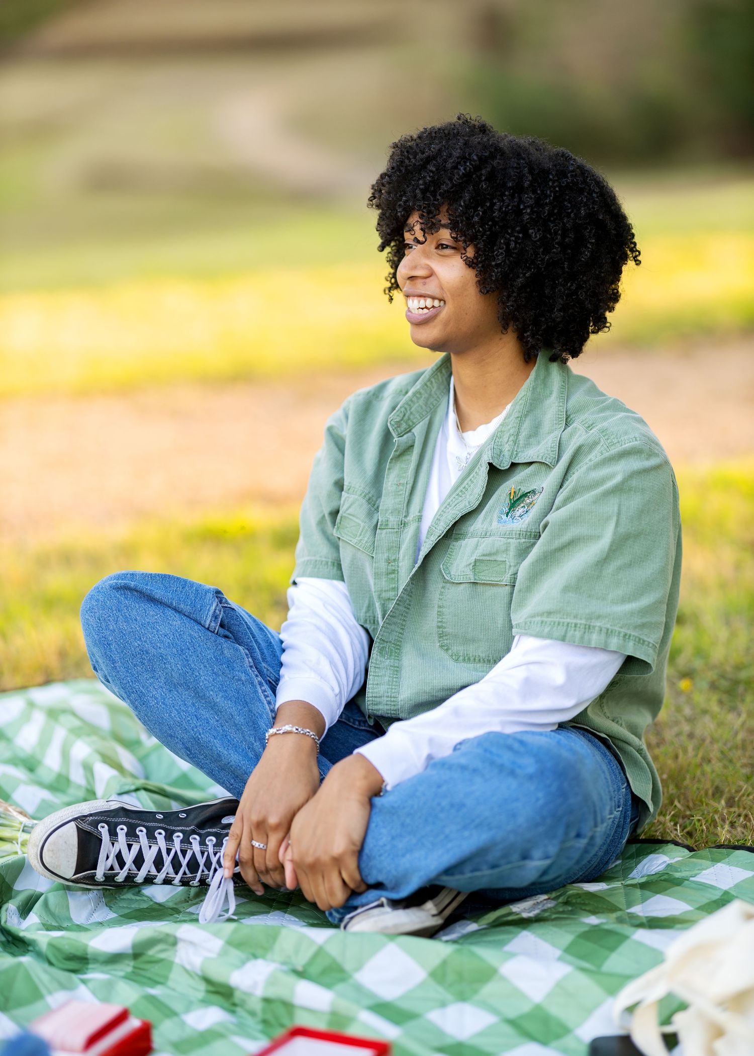 Person in mint green jacket and jeans relaxing on checkered blanket outdoors.