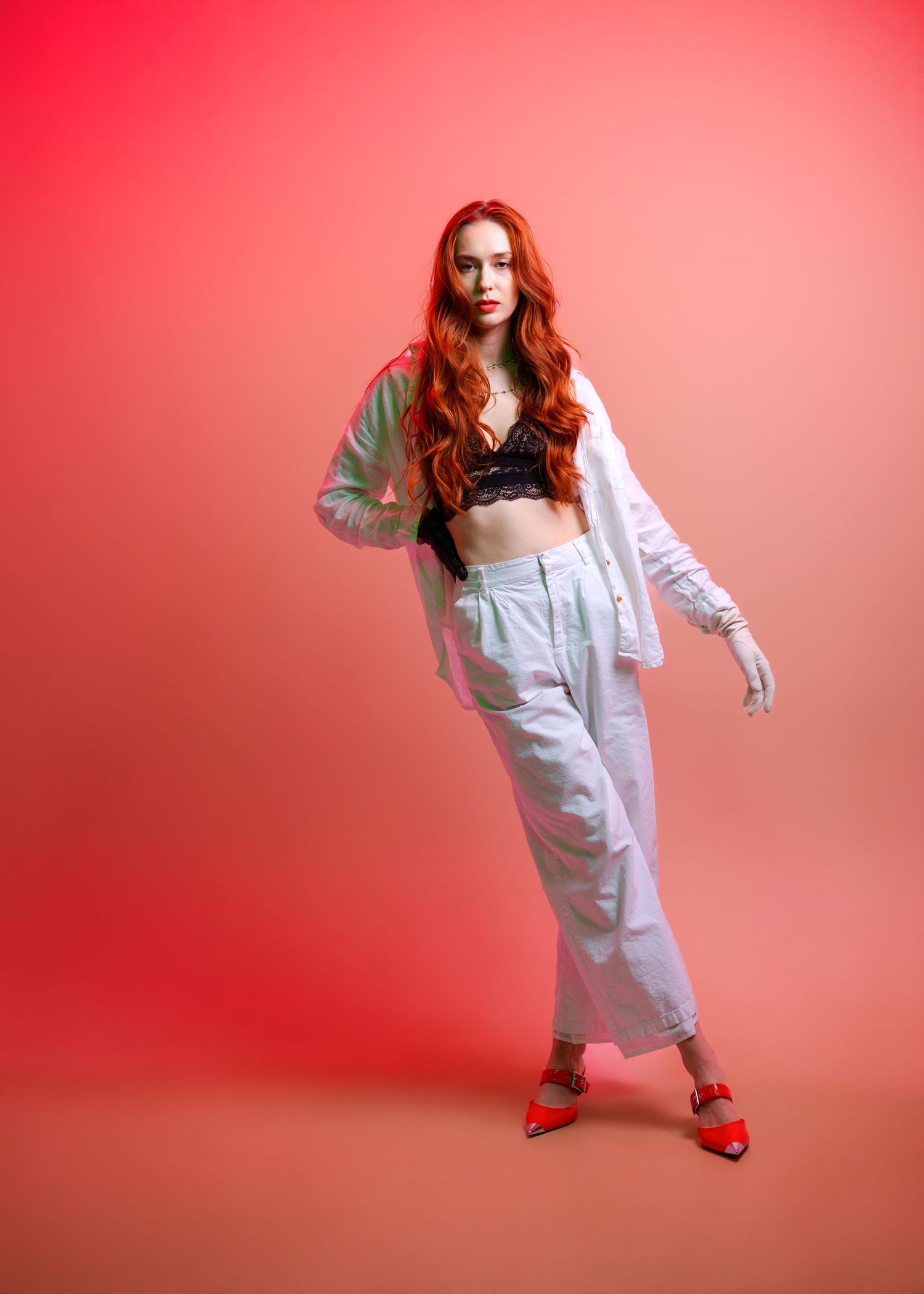 Figure in flowing white dress poses dynamically against vibrant red studio backdrop.