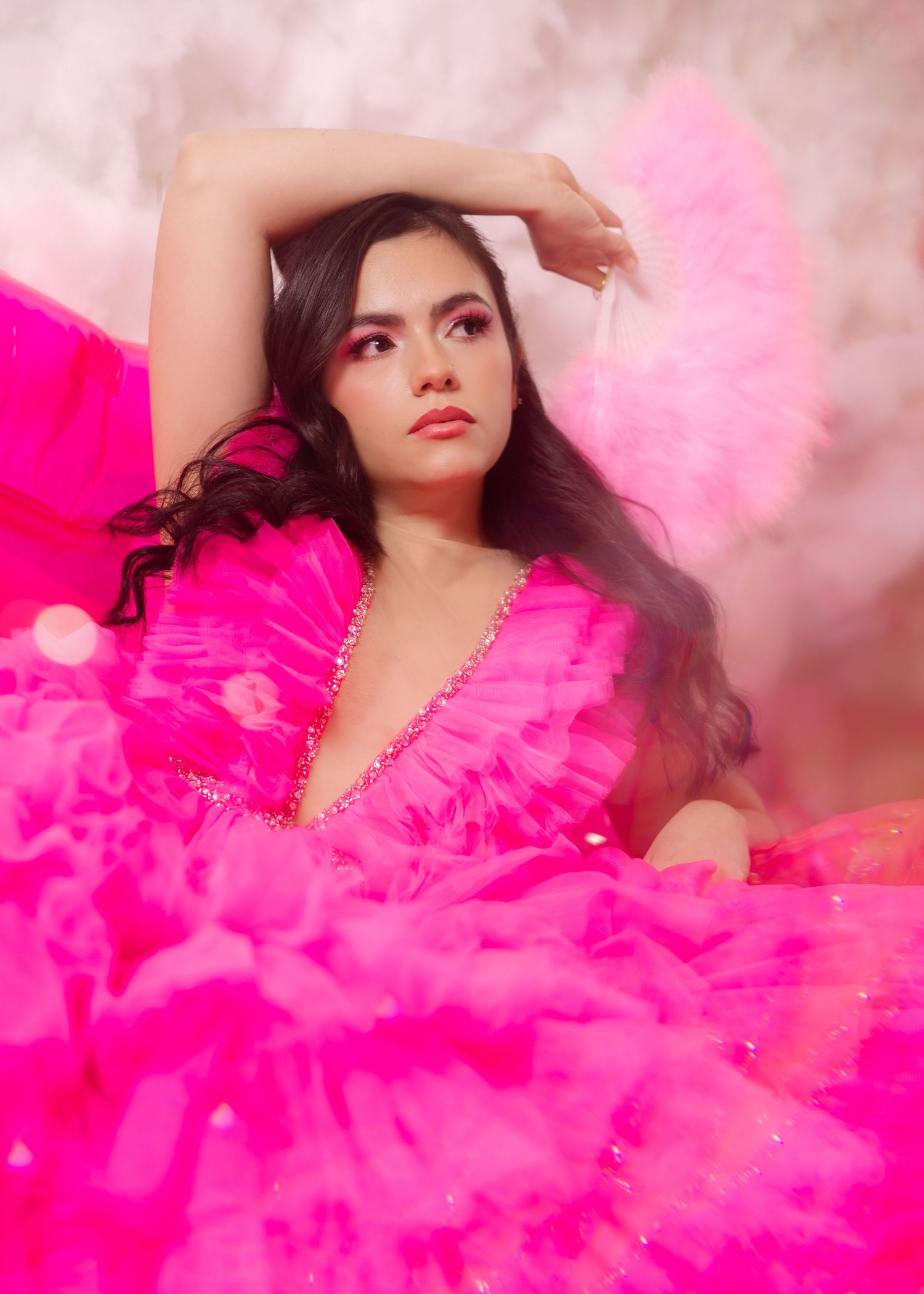 A dreamy fashion portrait with flowing hot pink tulle fabric creating an ethereal effect against a soft pink background.