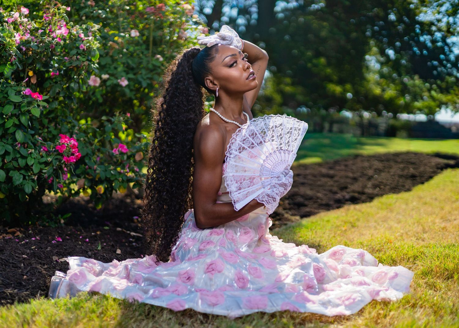 A pink floral dress flows gracefully across a sunny garden lawn with vibrant flowers in the background.