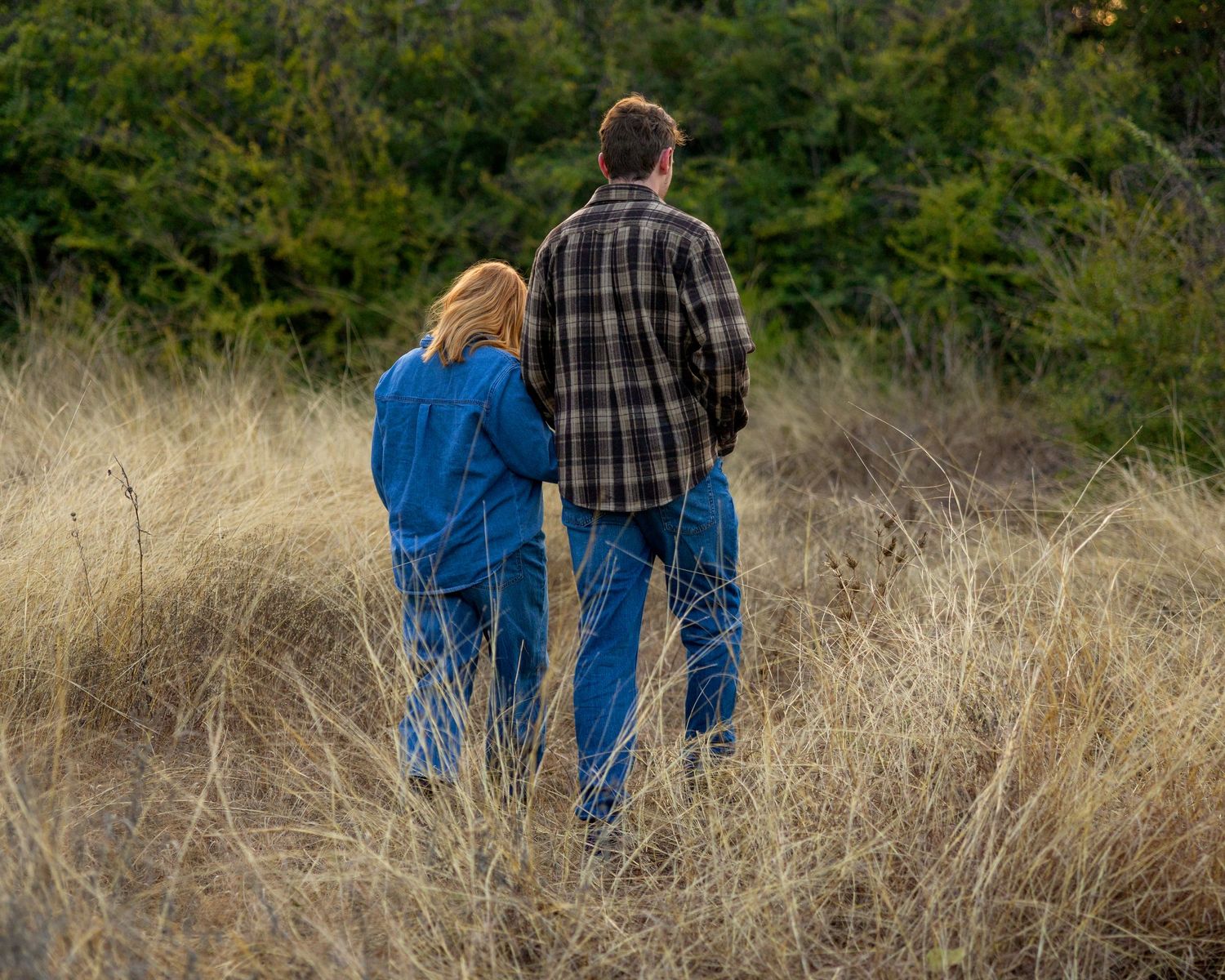 Couple walking through tall grass field during golden hour.