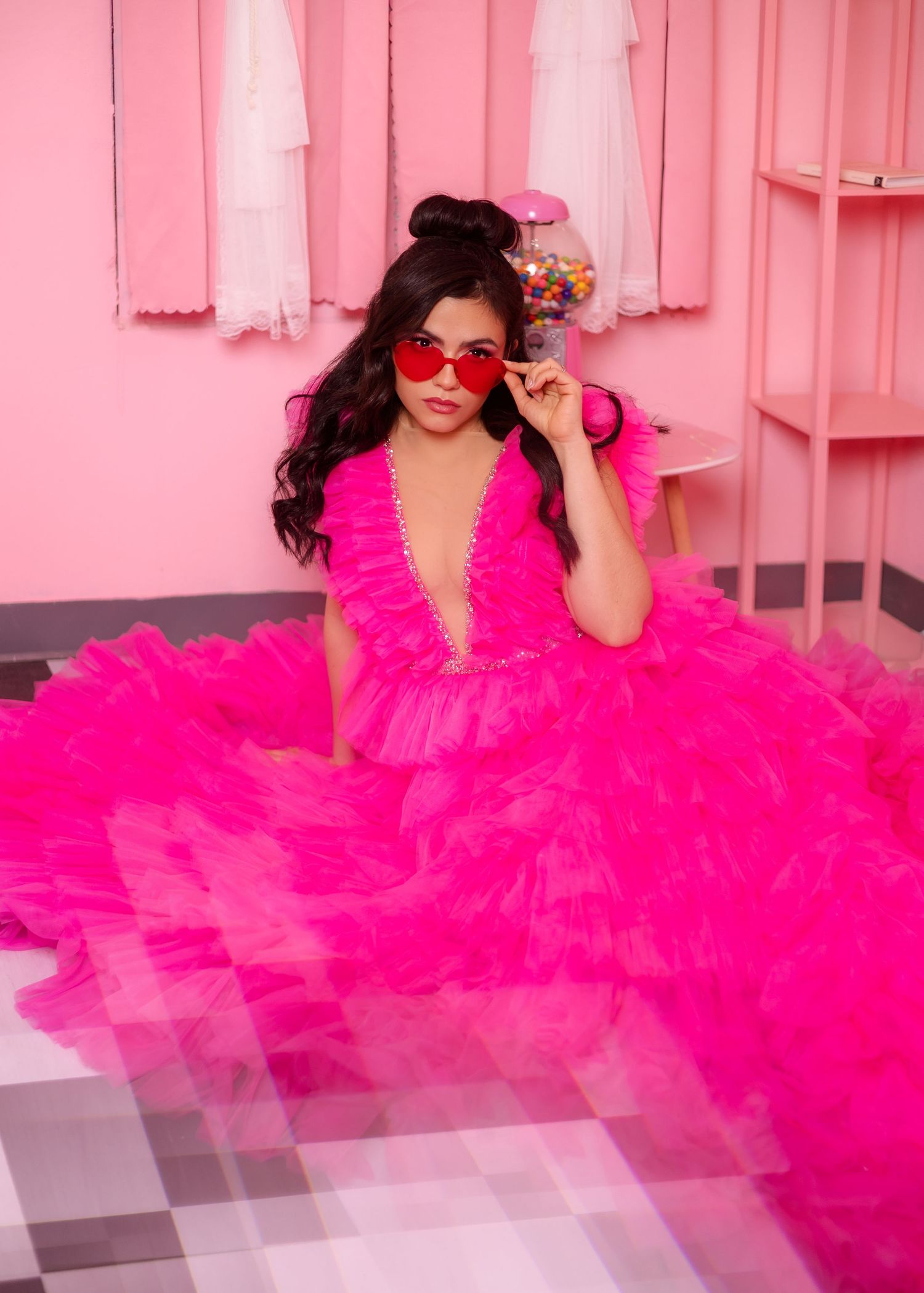 Model in vibrant pink tulle gown wearing red sunglasses in an all-pink room setting.