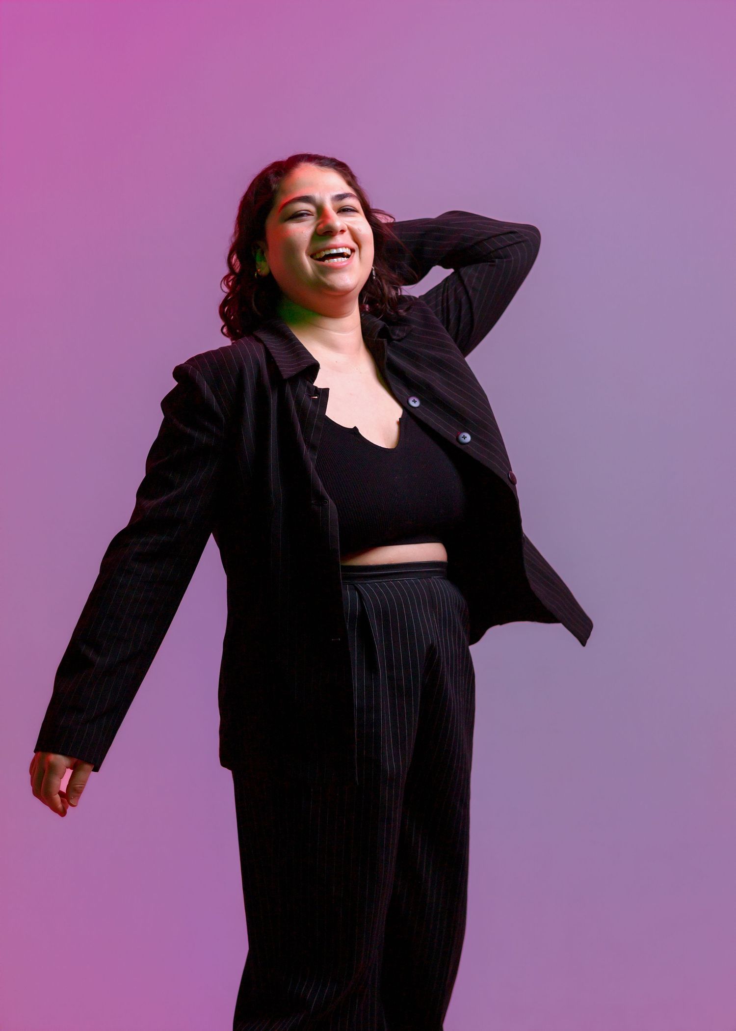 Woman in black blazer and pants laughing joyfully against purple gradient background.