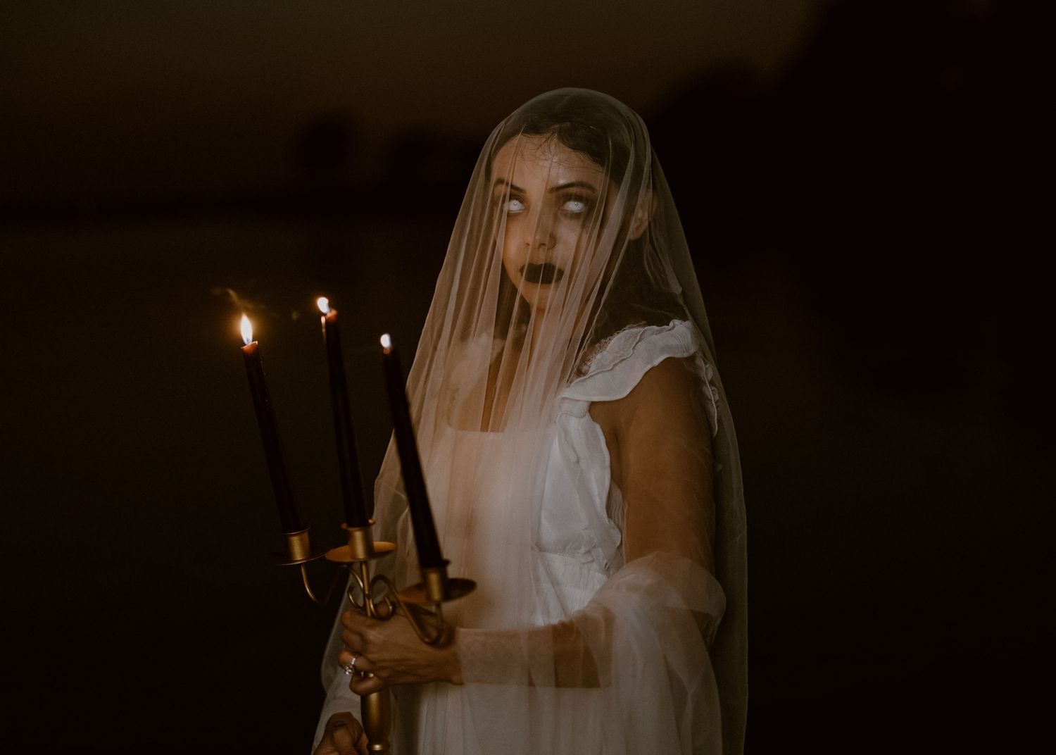 A moody nighttime scene with ethereal figures holding candles creates a mystical atmosphere.