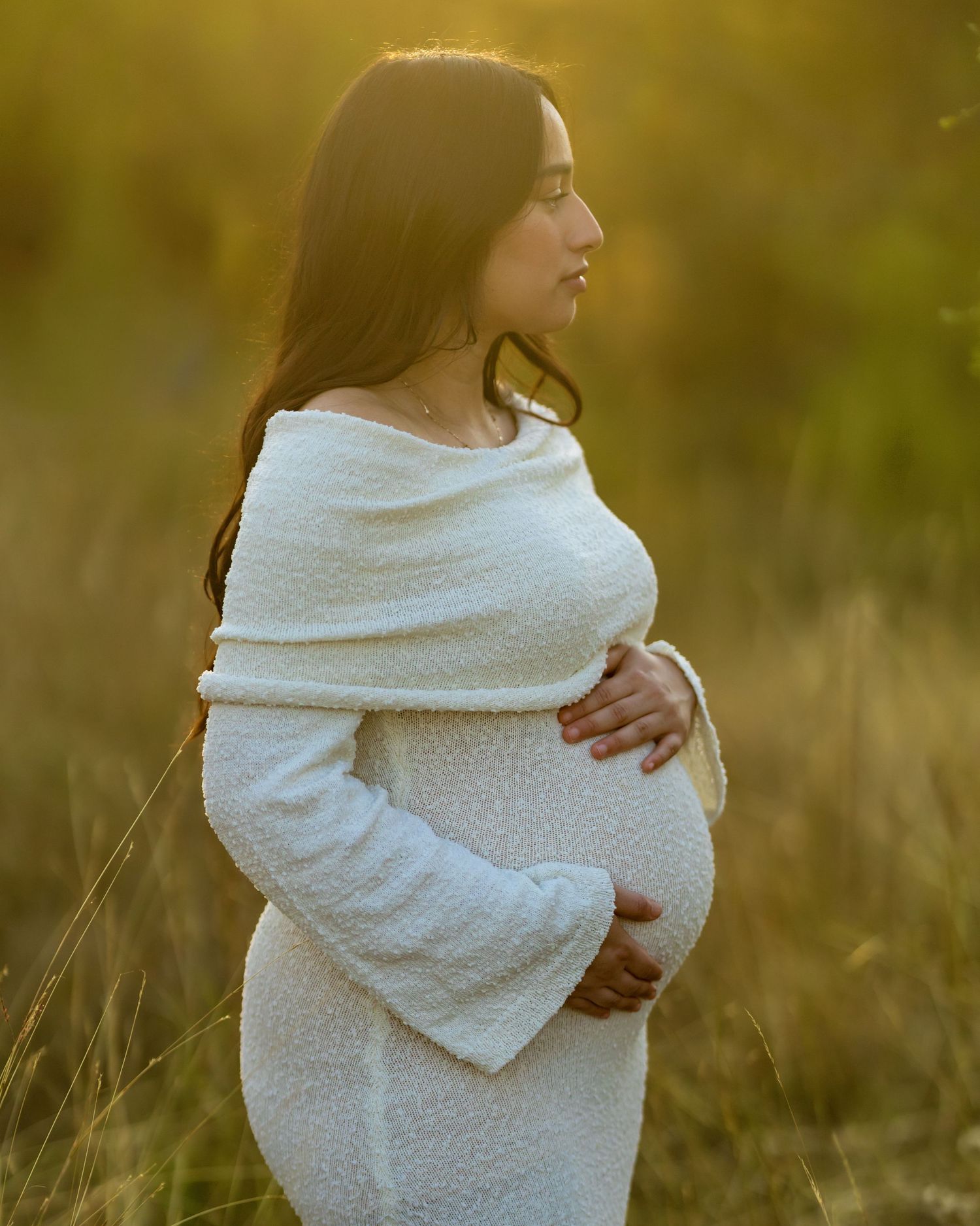 Side view maternity portrait in white dress during sunset in tall grass.