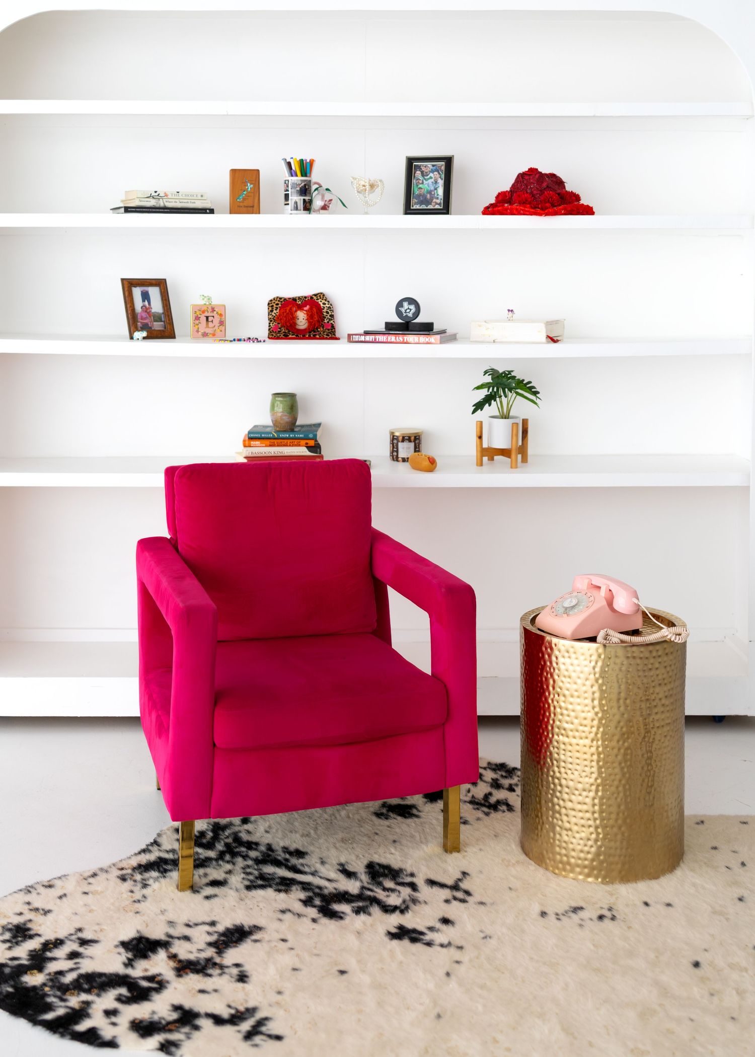 A bright pink armchair sits next to a gold side table on a beige carpet with black floral patterns.