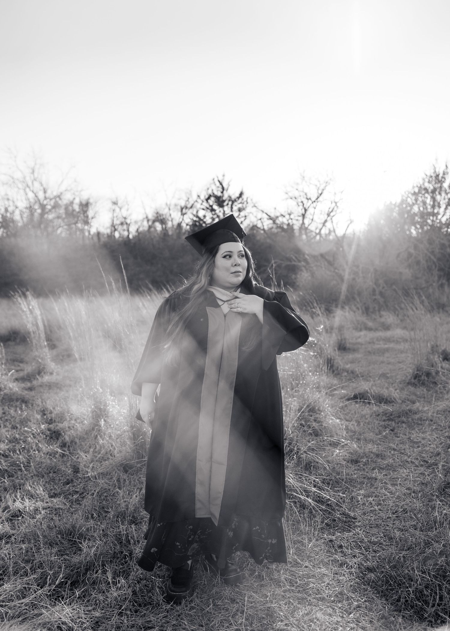A figure in a black coat stands in a misty field with sunlight creating an ethereal atmosphere in black and white.