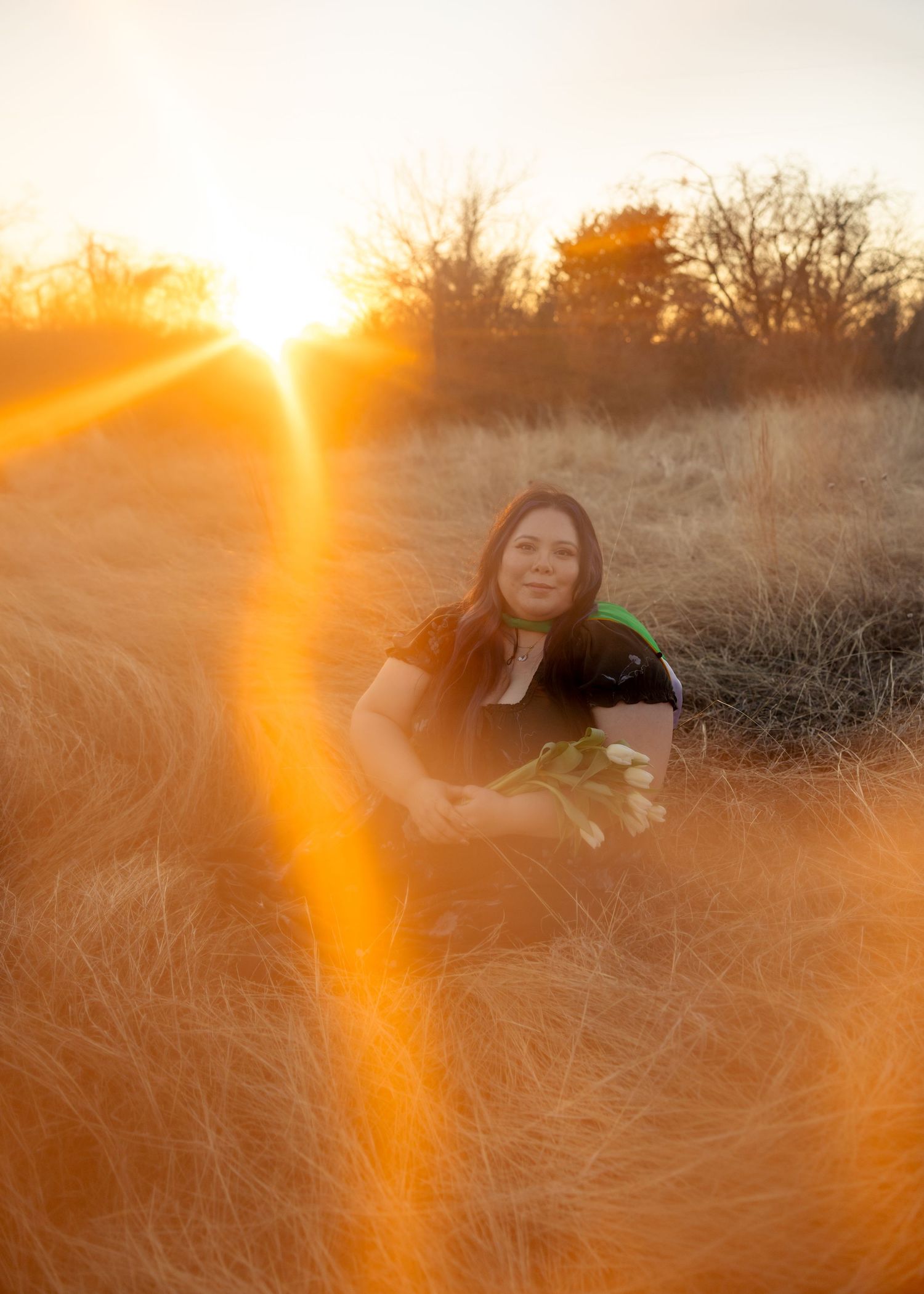 A person lying in tall golden grass during sunset creating a dreamy atmospheric scene with warm sunlight flares.