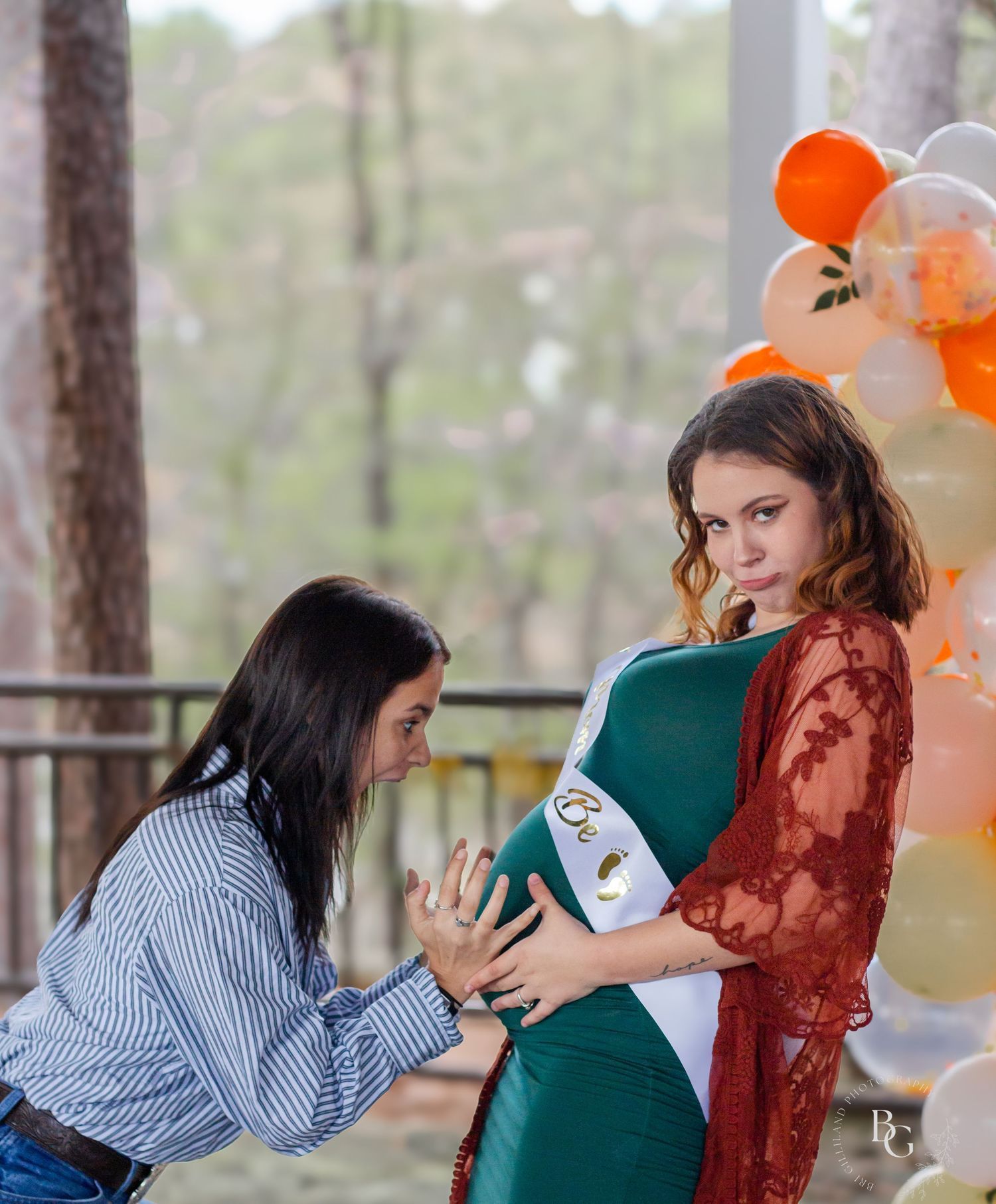 Baby shower scene with person touching pregnant belly decorated with orange balloons.